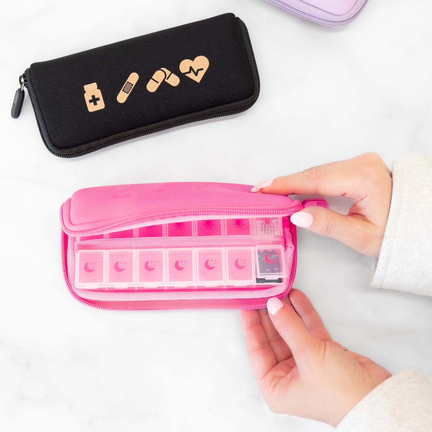 Someone opens a pink MyTagAlongs Icons Vitamin Organizer pouch on a white surface.