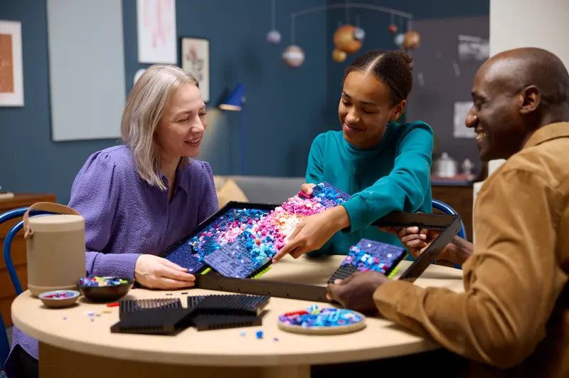 Lifestyle image of three adults sitting at a table working on assembling the LEGO Milky Way Galaxy set.