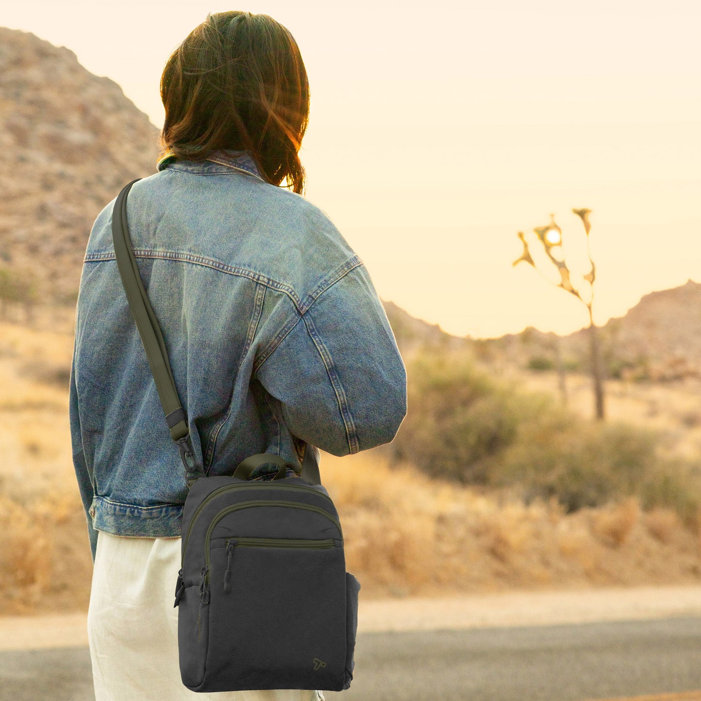 Lifestyle image of back view of person outside wearing a jean jacket and black Travelon Voyages Anti-Theft Tour Bag.