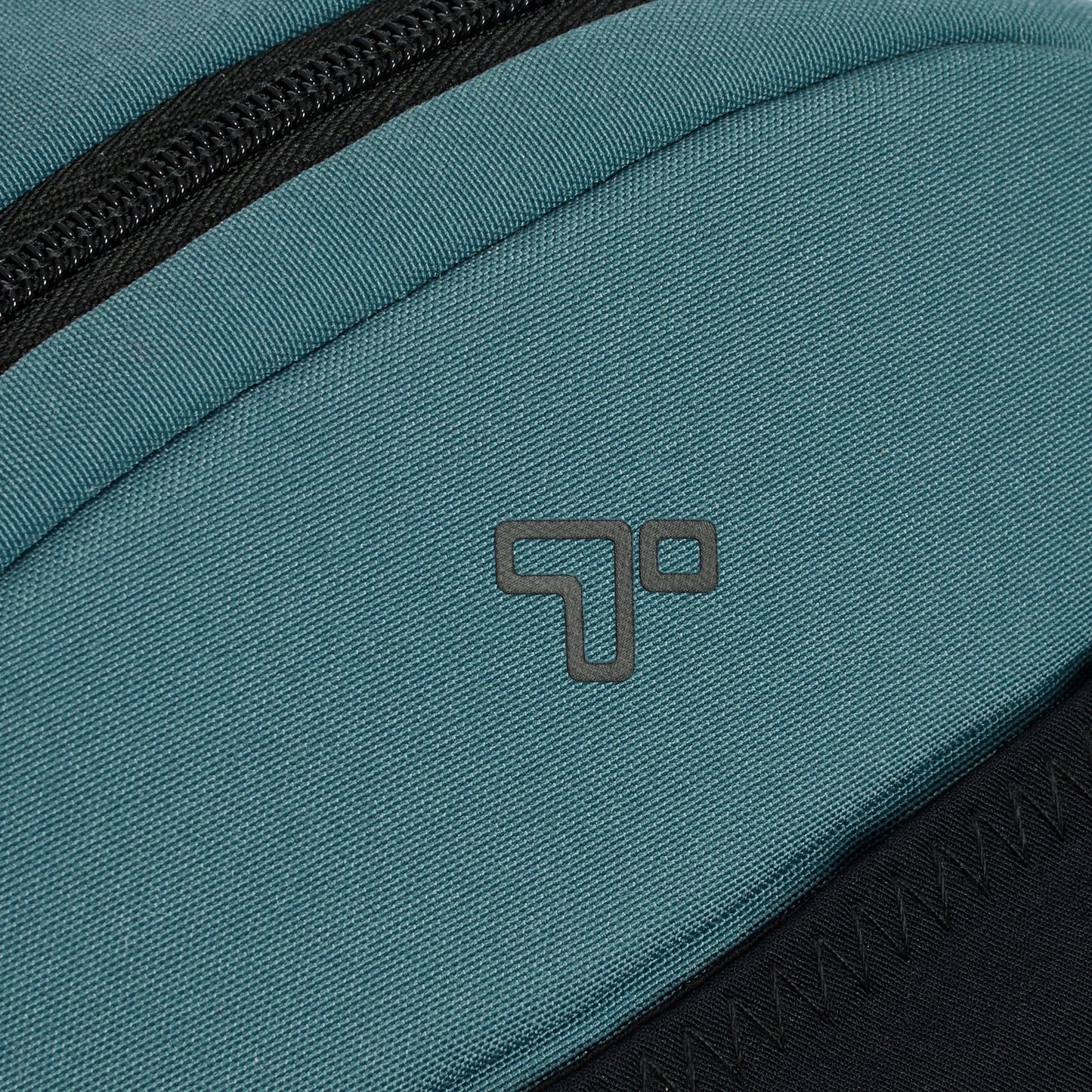 Close-up of the slate blue Travelon Voyages Anti-Theft Small Backpack, showcasing a black zipper and geometric logo.