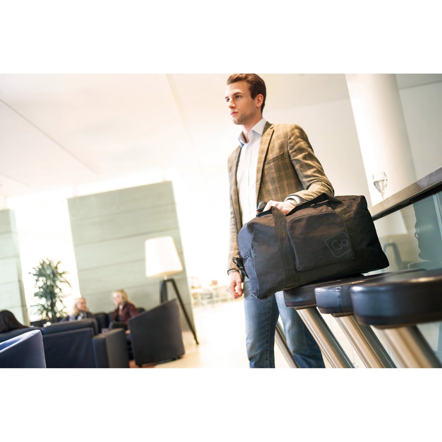 Lifestyle image of man in an airport lounge with the black Go Travel Classic Foldaway Travel Bag resting on a chair beside him