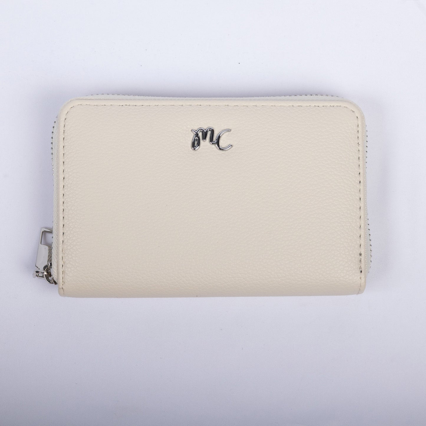 The Miss Caprice Zip Around Wallet is a small white vegan leather wallet with a silver "MC" emblem and zipper.
