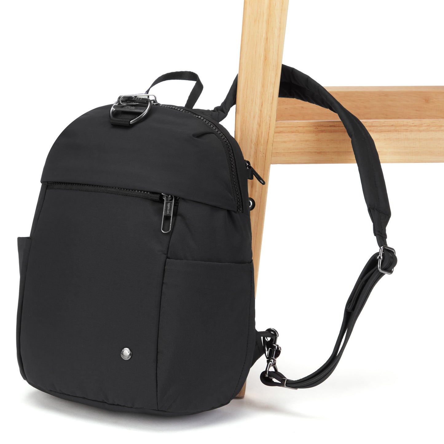A black Pacsafe® CX Anti-theft 8L Backpack Petite with zippers and straps hangs on a wooden chair.