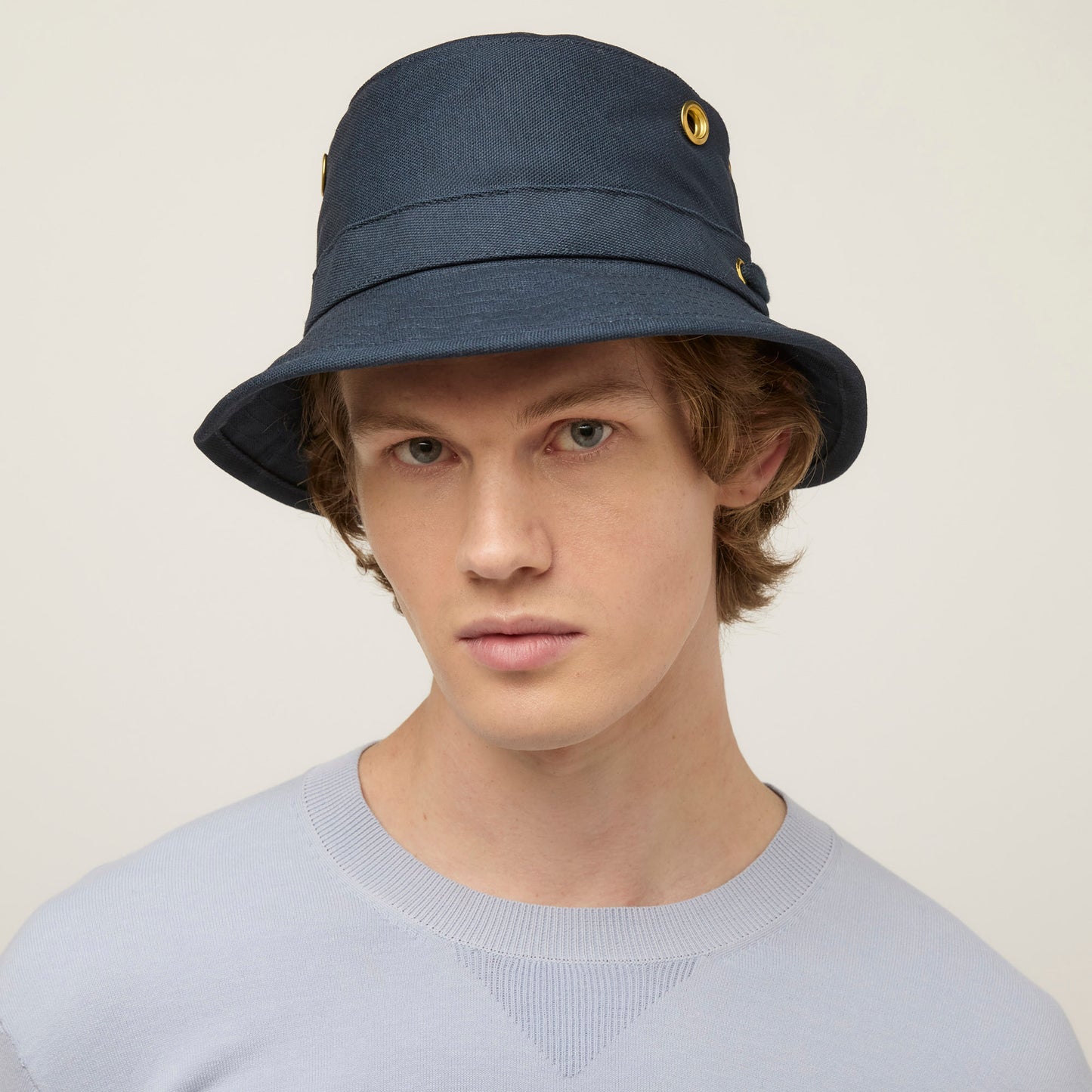 A young person in a navy Tilley T1 Iconic Bucket Hat and light grey sweatshirt, offering sun protection.