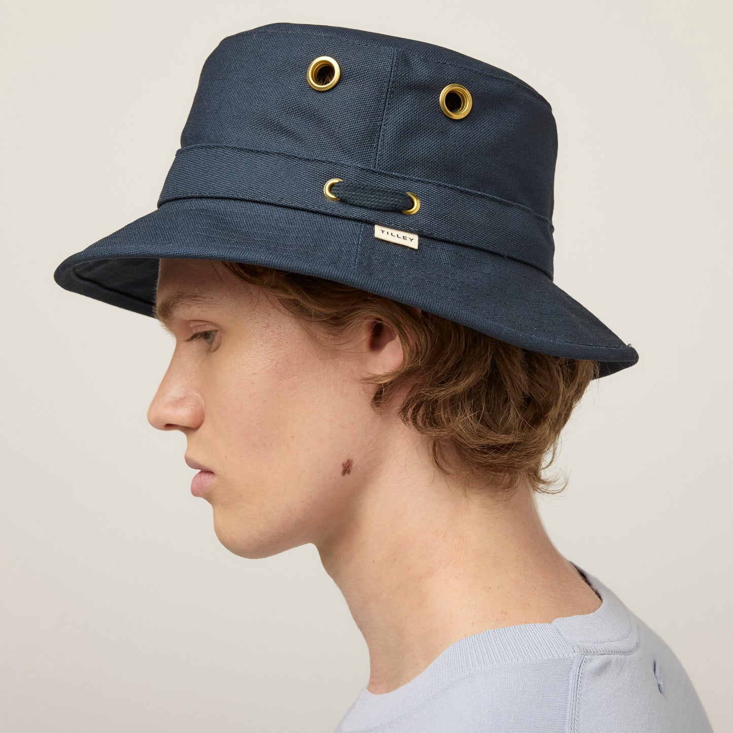 Person in profile wears a Tilley T1 Iconic Bucket Hat in navy and a light blue shirt against a plain background.