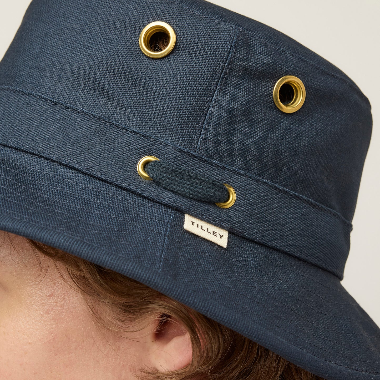 Close-up of a person wearing the Tilley T1 Iconic Bucket Hat, featuring gold eyelets and signature label.