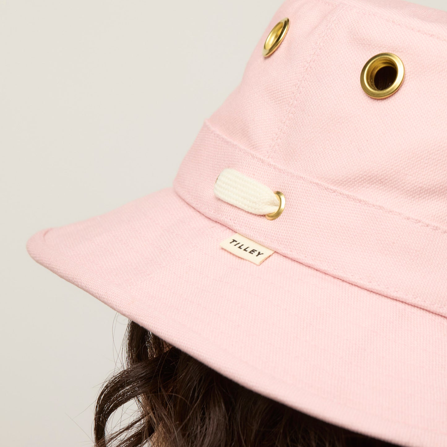Close-up of the Tilley T1 Iconic Bucket Hat in pink, with grommets, worn by someone with brown wavy hair.