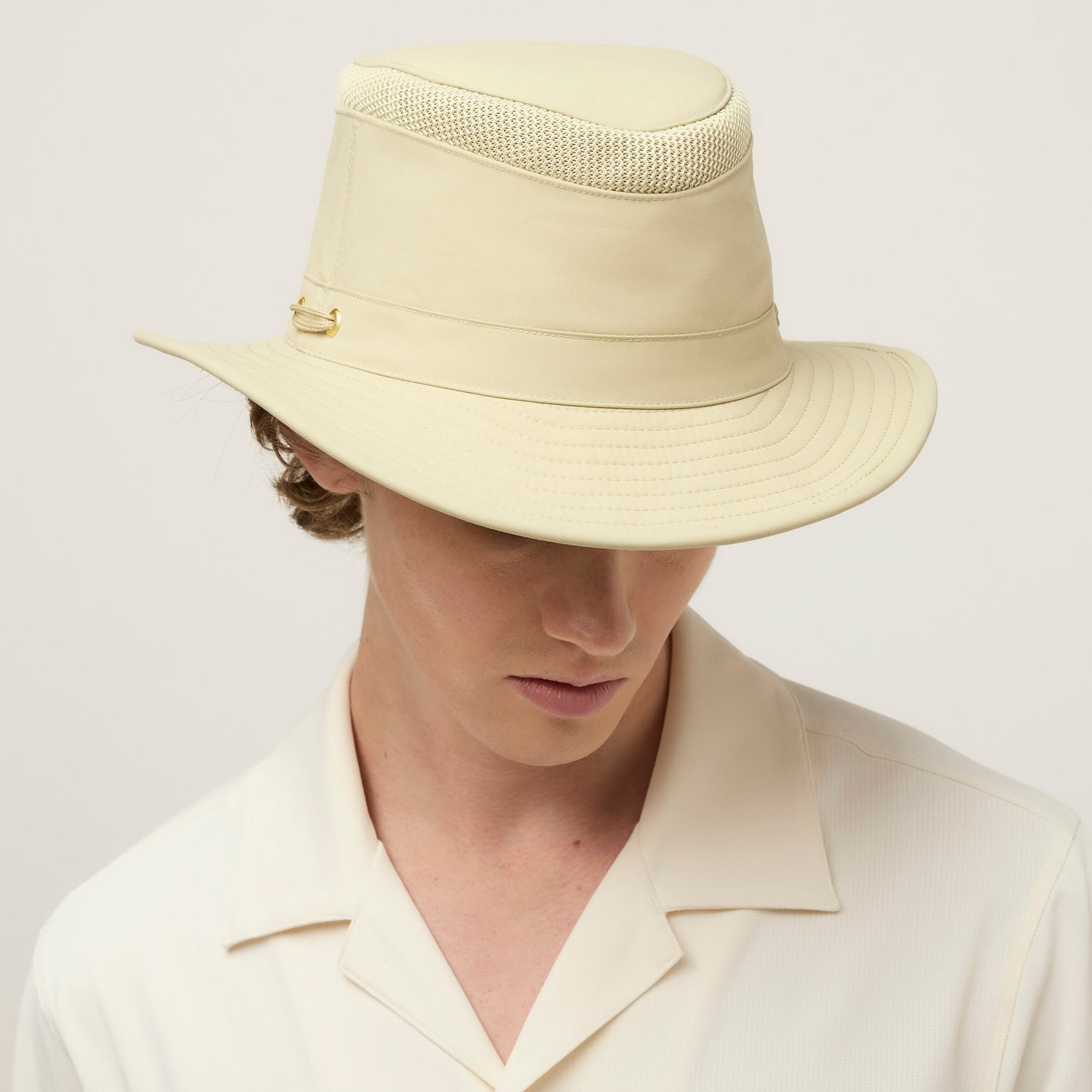 Person in a cream collared shirt and a Tilley LTM5 Airflo® Hat, looking down.