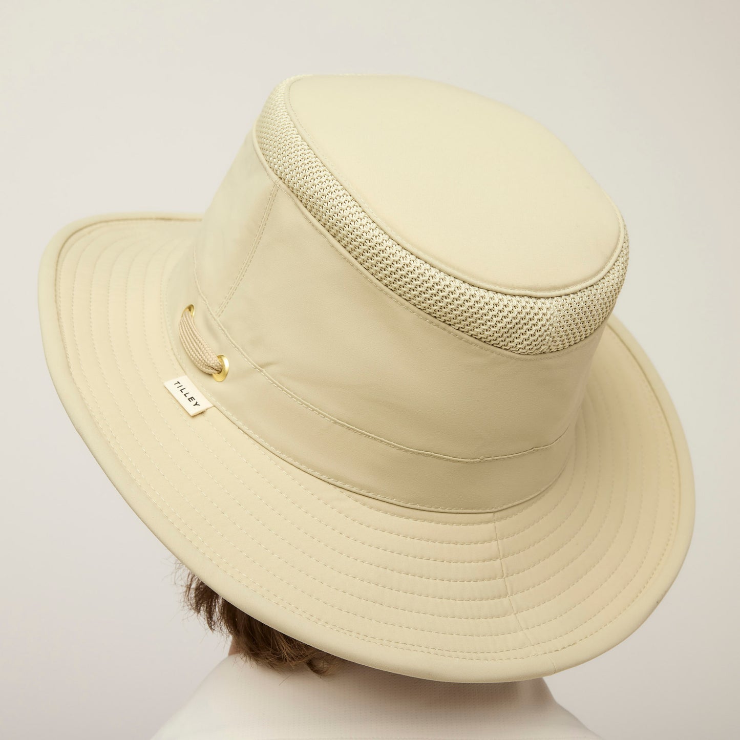 A person wears a Tilley LTM5 Airflo® Hat, a sun-blocking beige hat with ventilation and a small side label.