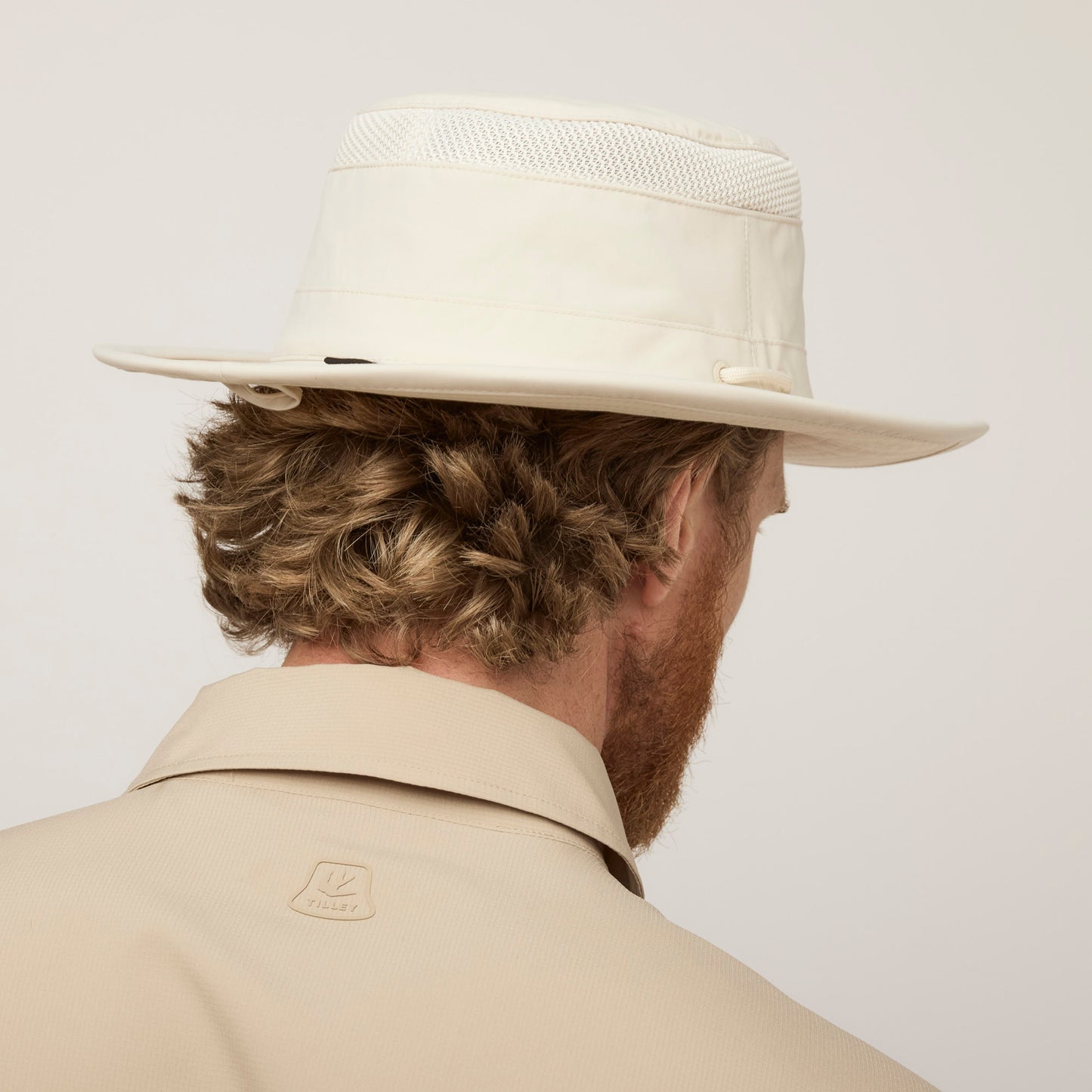 A man shown from behind wears a Tilley Airflo® Boonie Hat and a beige collared jacket.