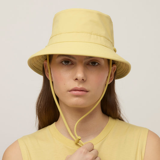 Product Image – Someone wearing a light yellow Tilley LTM1 Airflo® Bucket Hat with chin strap and matching sleeveless top, facing forward.