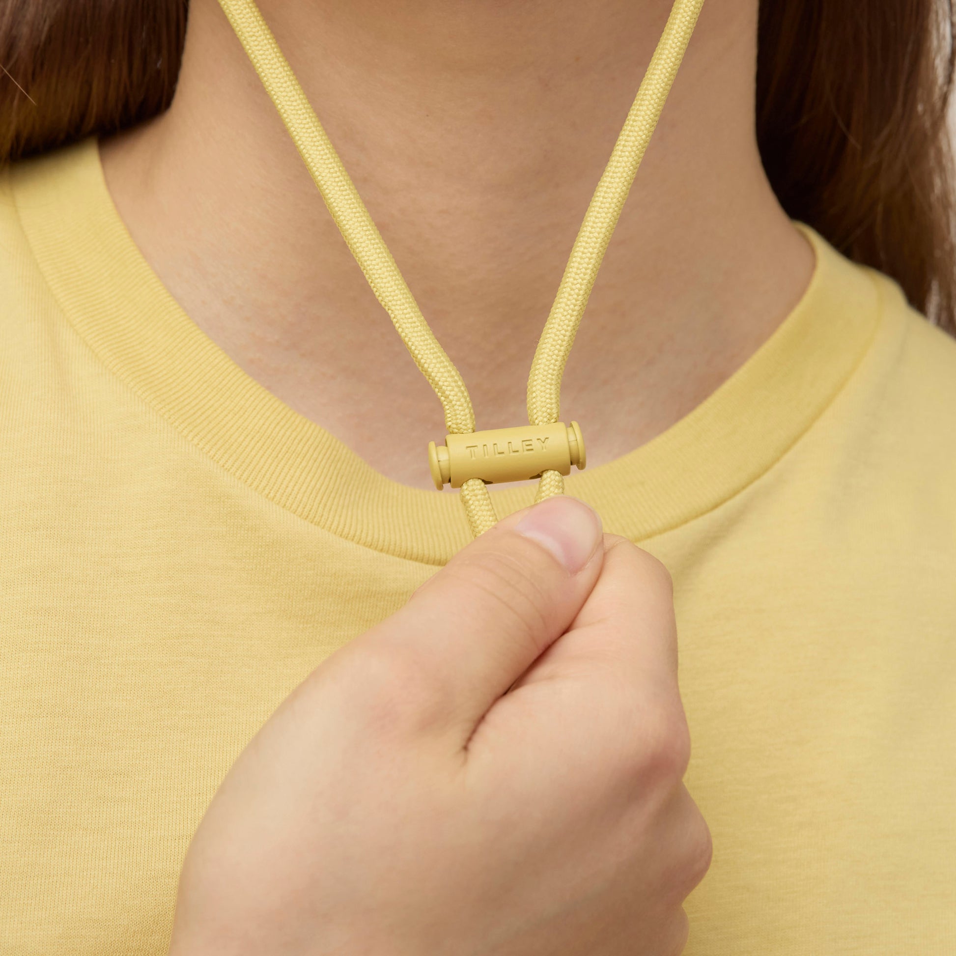 A hand adjusts a yellow cord lock labeled "TILLEY" on the Tilley LTM1 Airflo® Bucket Hat.