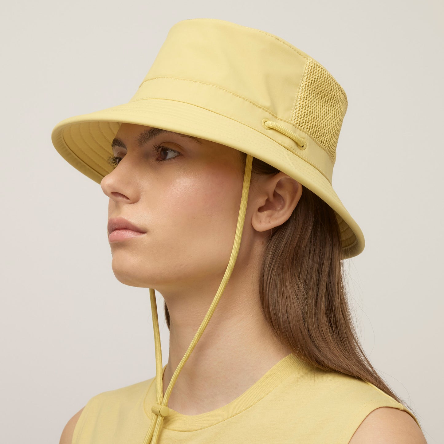 Person wearing a light yellow Tilley LTM1 Airflo® Bucket Hat with mesh panel and chin strap, in profile.