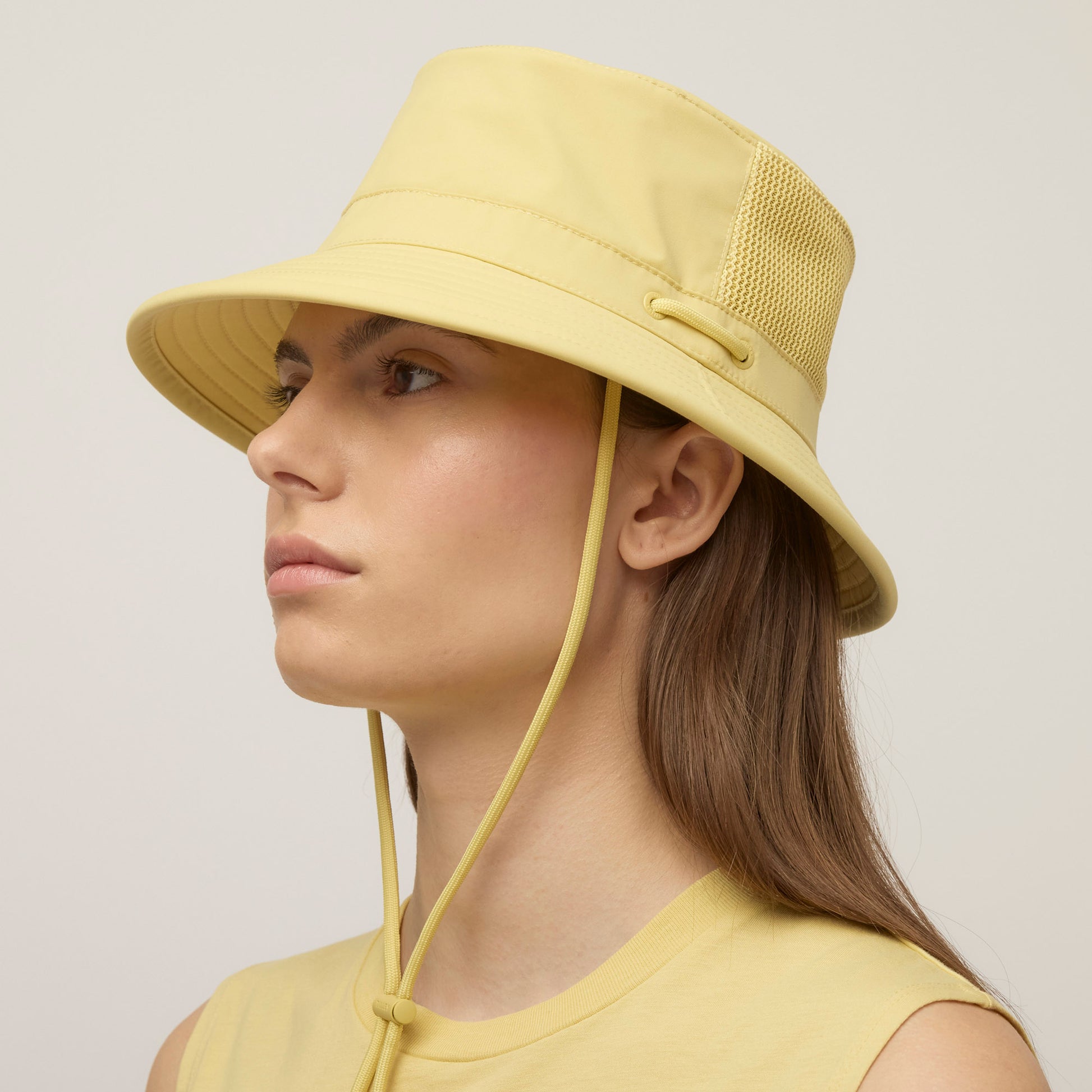 Person wearing a light yellow Tilley LTM1 Airflo® Bucket Hat with mesh panel and chin strap, in profile.