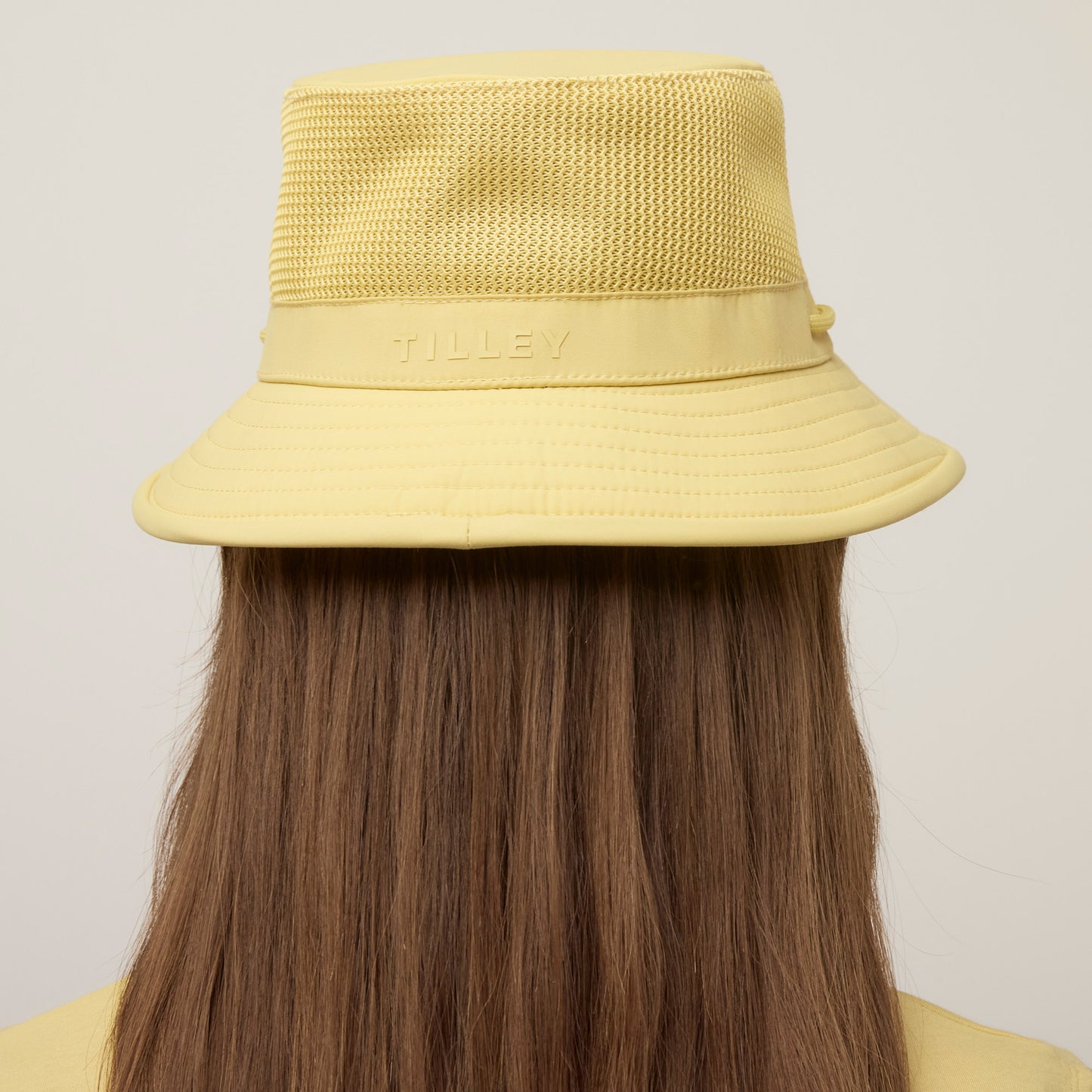 Person with long brown hair wearing a yellow Tilley LTM1 Airflo® Bucket Hat, viewed from the back.
