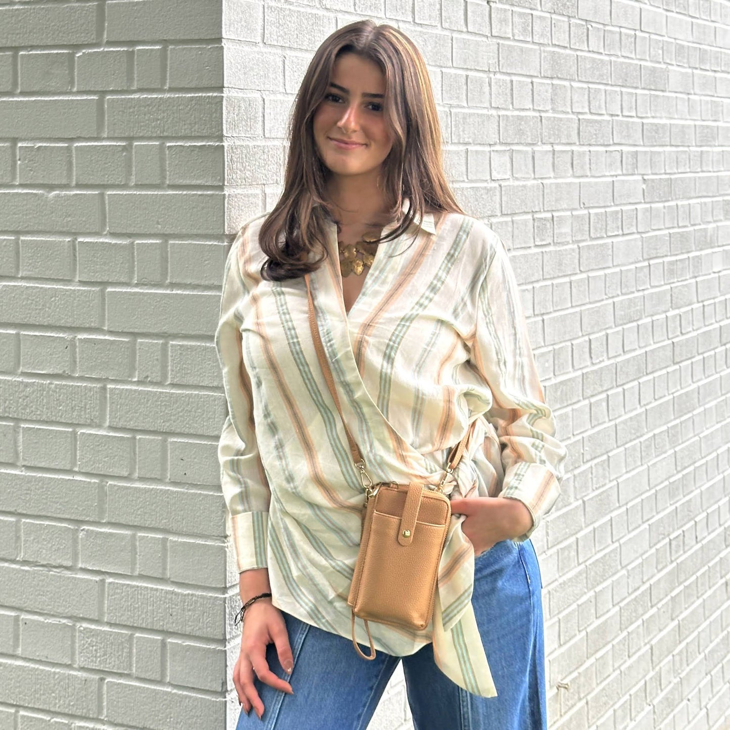 A person in a striped shirt and jeans holds an Espe Pastel Smartphone Pouch against a light brick wall.
