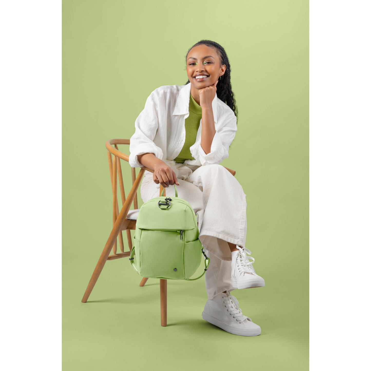 Someone in a white outfit sits with the Pacsafe® CX 8L backpack against a light green background.