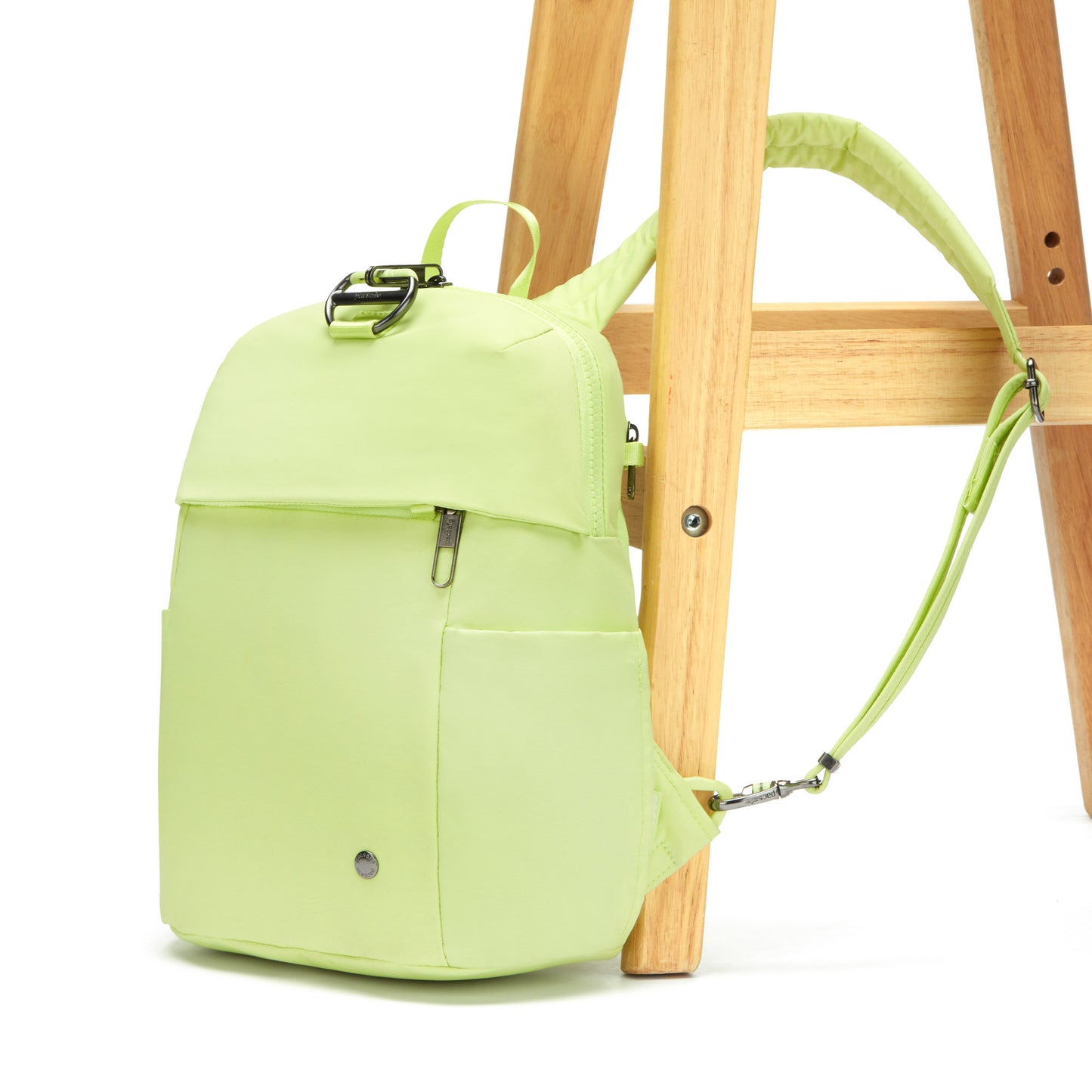 A matcha green Pacsafe anti-theft backpack rests on a wooden chair against a white backdrop.