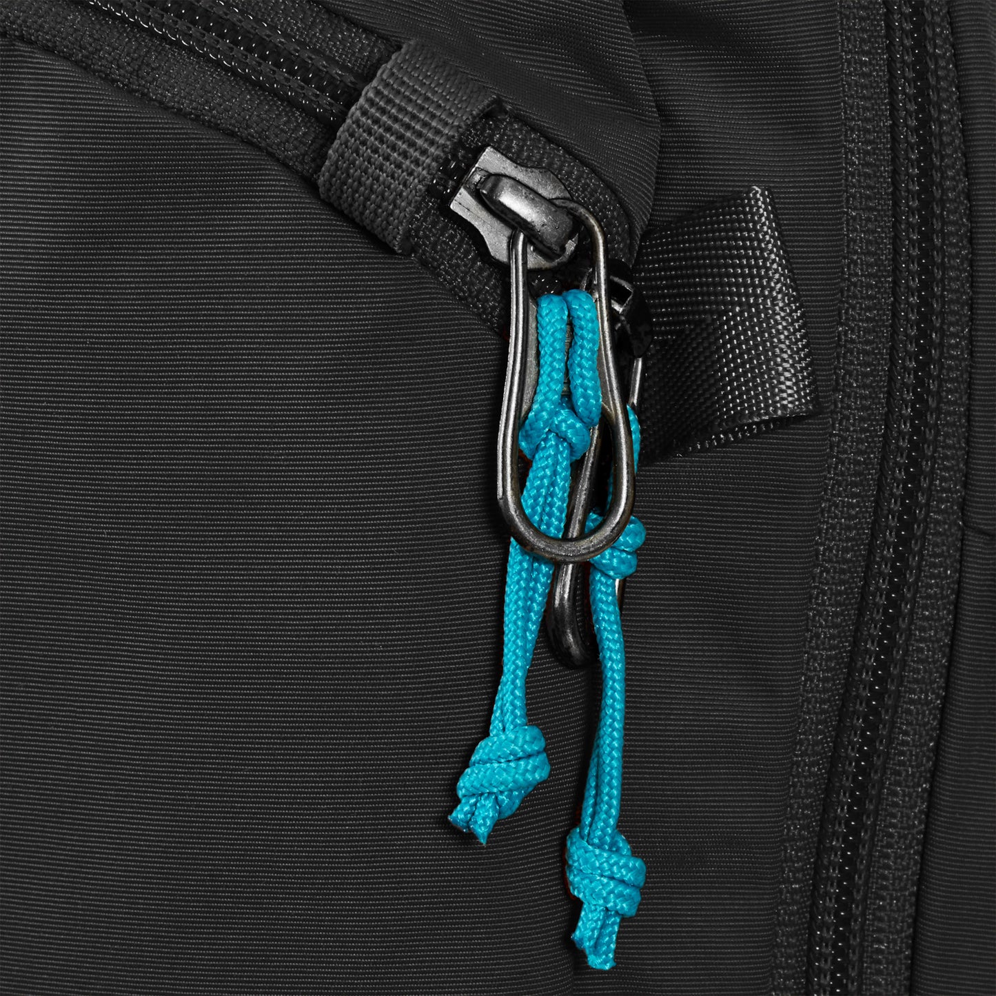 Close-up of Pacsafe® ECO 12L anti-theft sling backpack zipper, featuring blue cord pulls and metal clip, made from recycled materials.