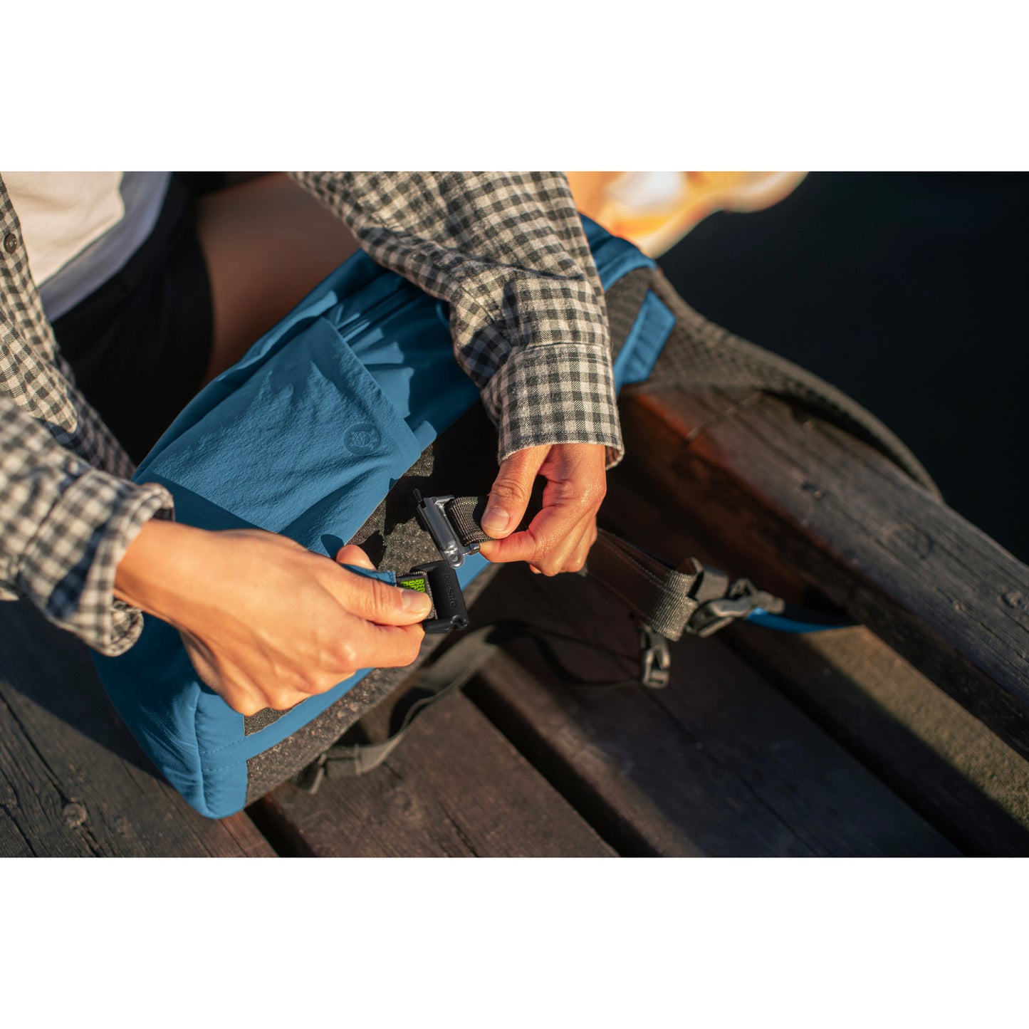 Lifestyle image of person clipping the Pacsafe® ECO 12L Anti-theft Sling Backpack in teal to a park bench.