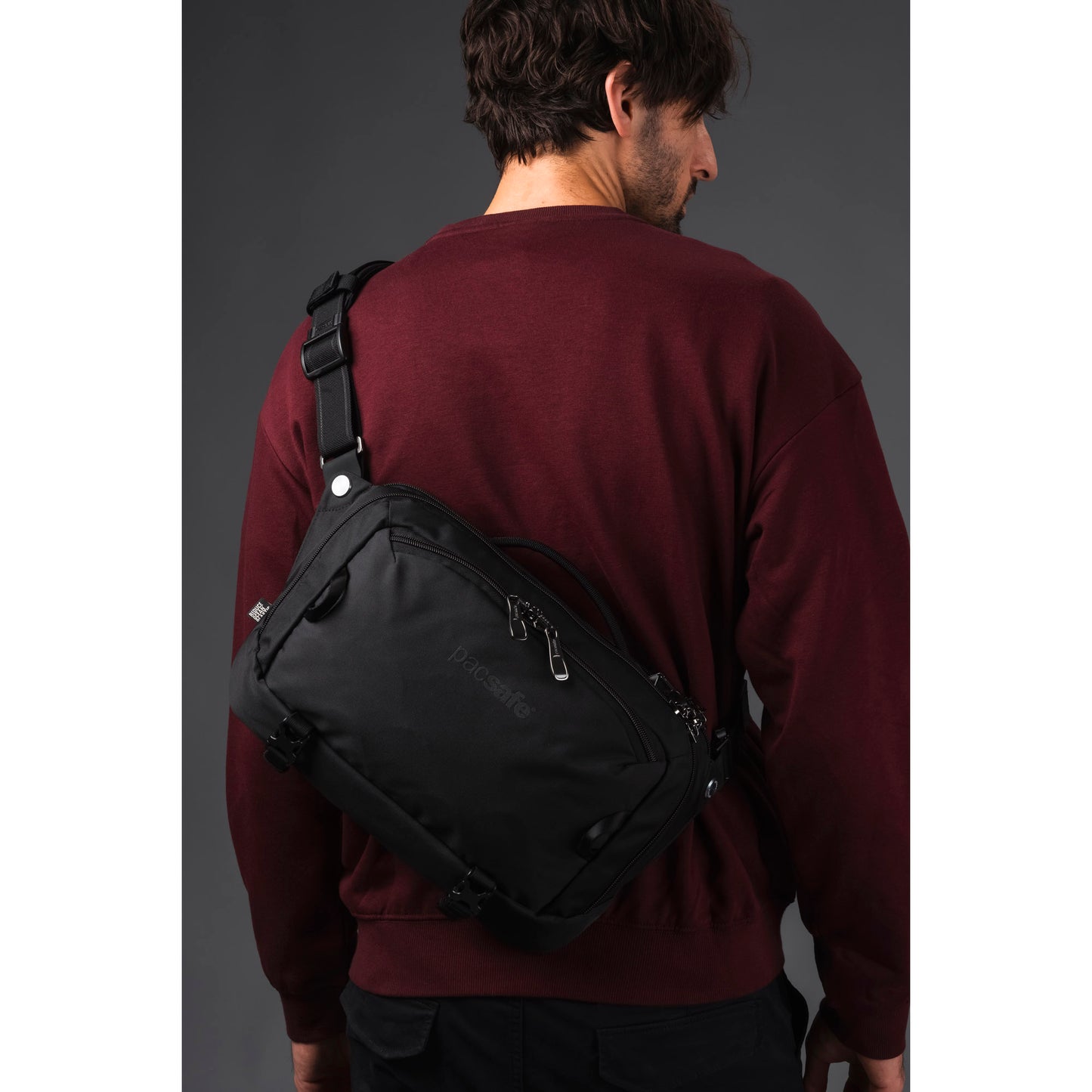 Person in a maroon sweatshirt with a Pacsafe® EXP 12 Anti-theft Sling Crossbody, against a gray background.