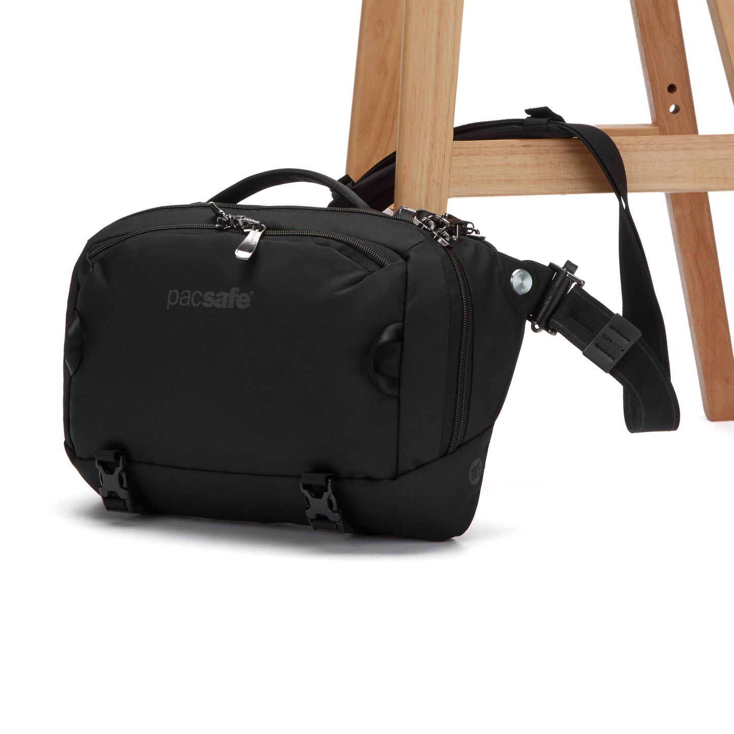 Pacsafe® EXP 12 Anti-theft Sling, recycled polyester black crossbody with zippers, on a wooden stool.