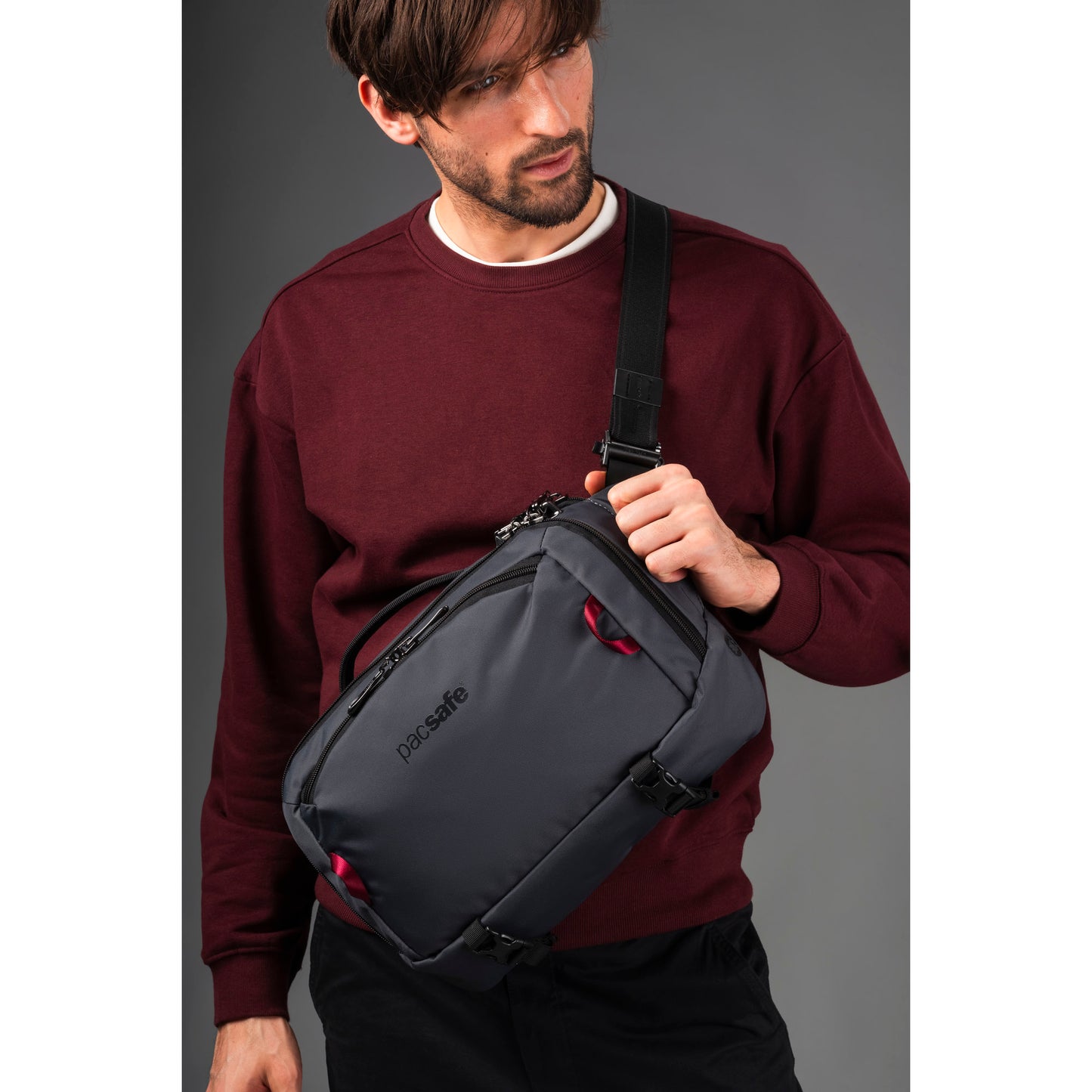 Man wearing a maroon sweater with the slate Pacsafe® EXP 12 Anti-theft Sling Crossbody across his front.