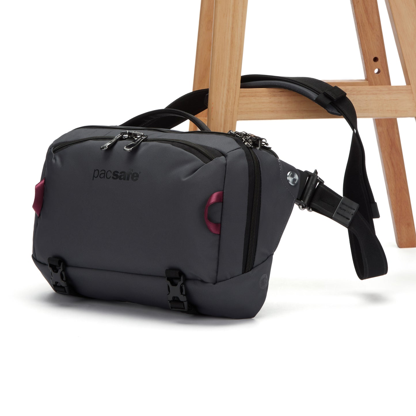 Pacsafe® EXP 12 Anti-theft Sling Crossbody in grey, clipped to a wooden chair leg.