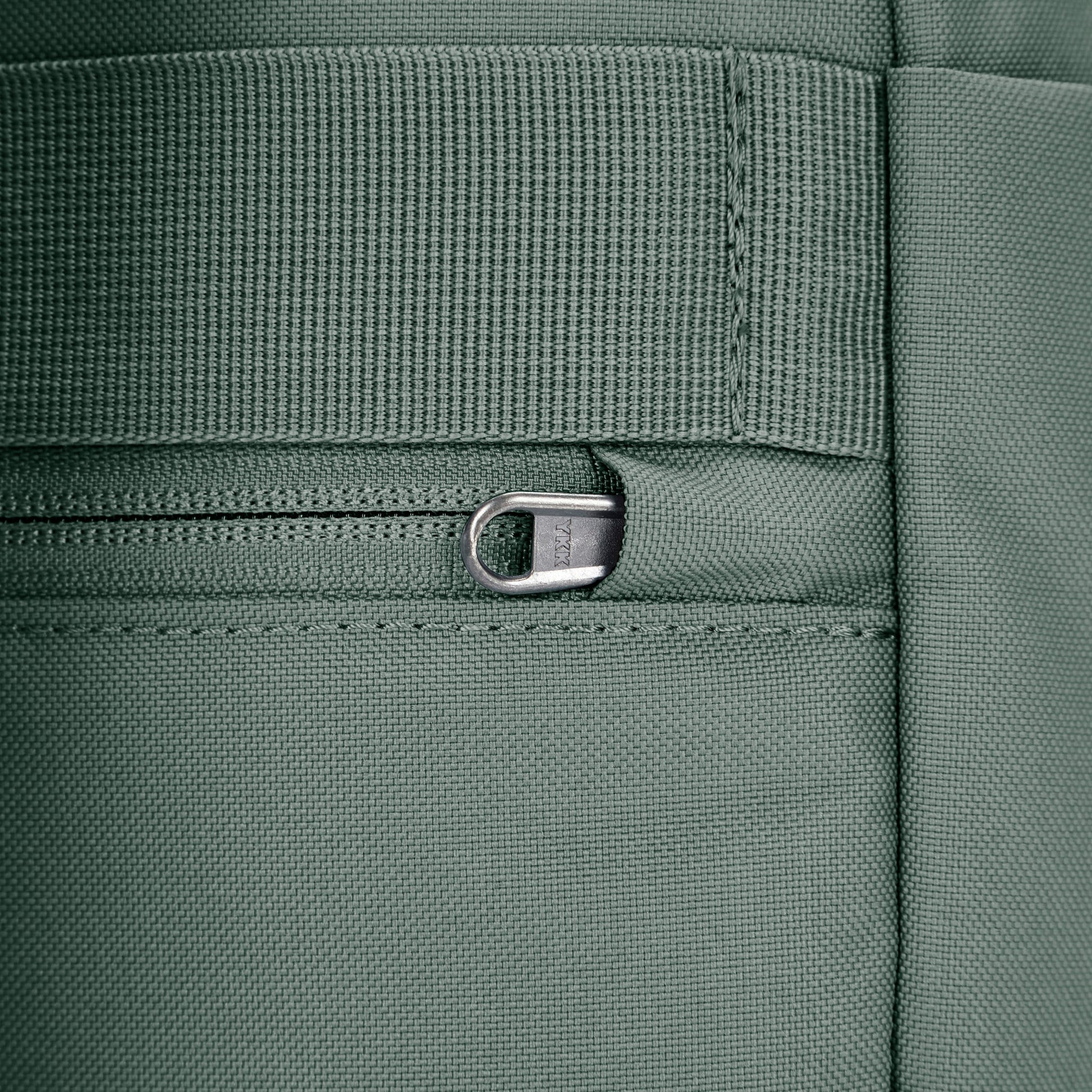 Close up of tucked zipper pull security feature on spruce green backpack