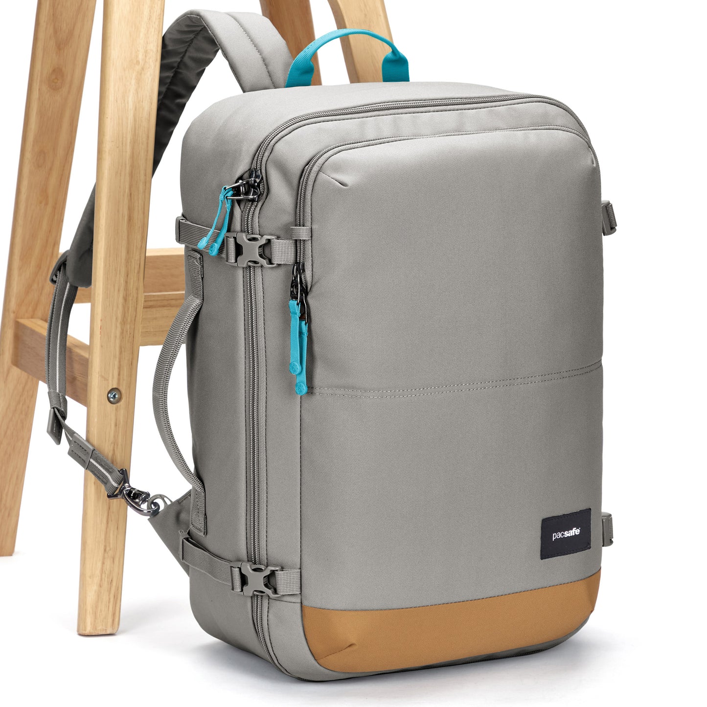 The Pacsafe® GO 34L Anti-theft Carry-on Backpack in gray and tan with blue pulls leans on a wooden chair.