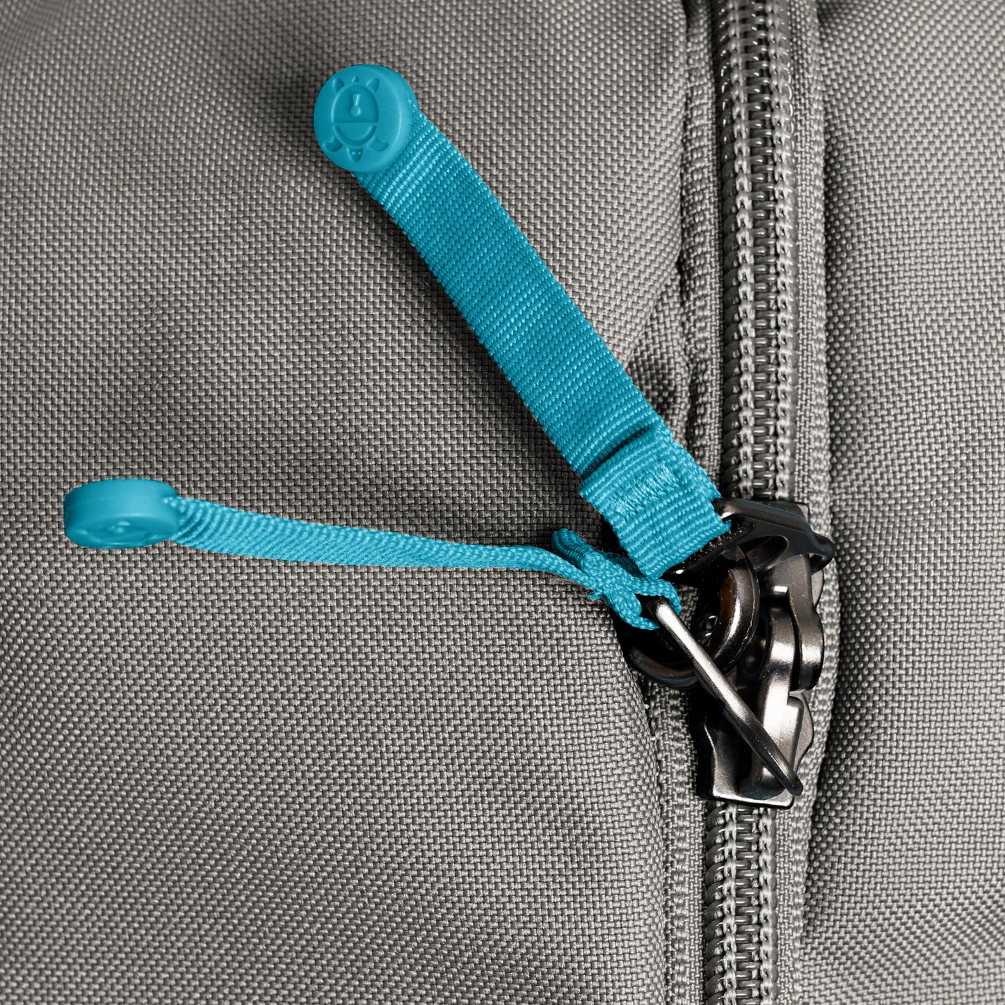 Close-up of a gray zipper with blue pull cords on the Pacsafe® GO 44L Anti-theft Carry-on Backpack.