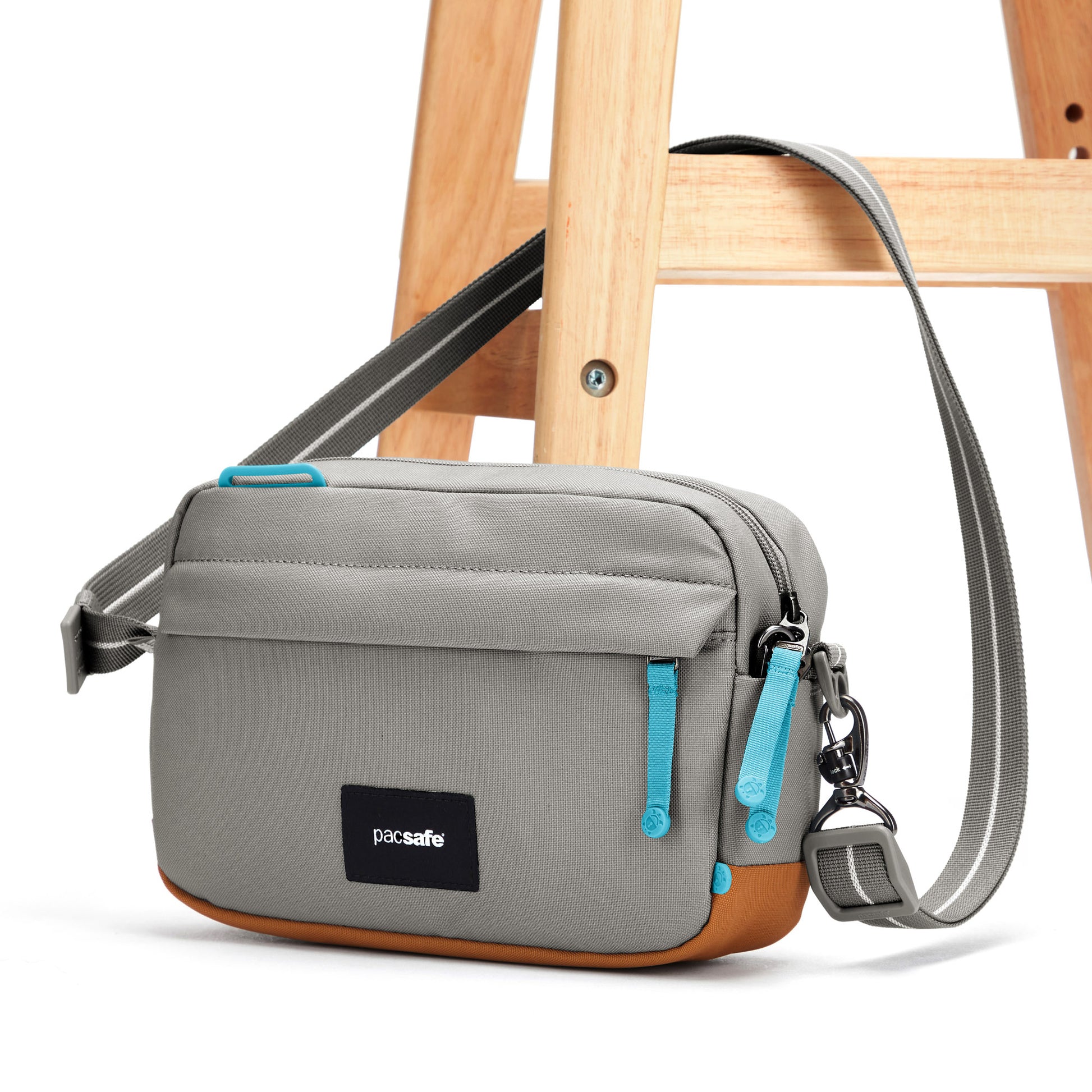Pacsafe® GO Anti-Theft Crossbody Bag, stone, with crossbody strap affixed through wooden chair leg.