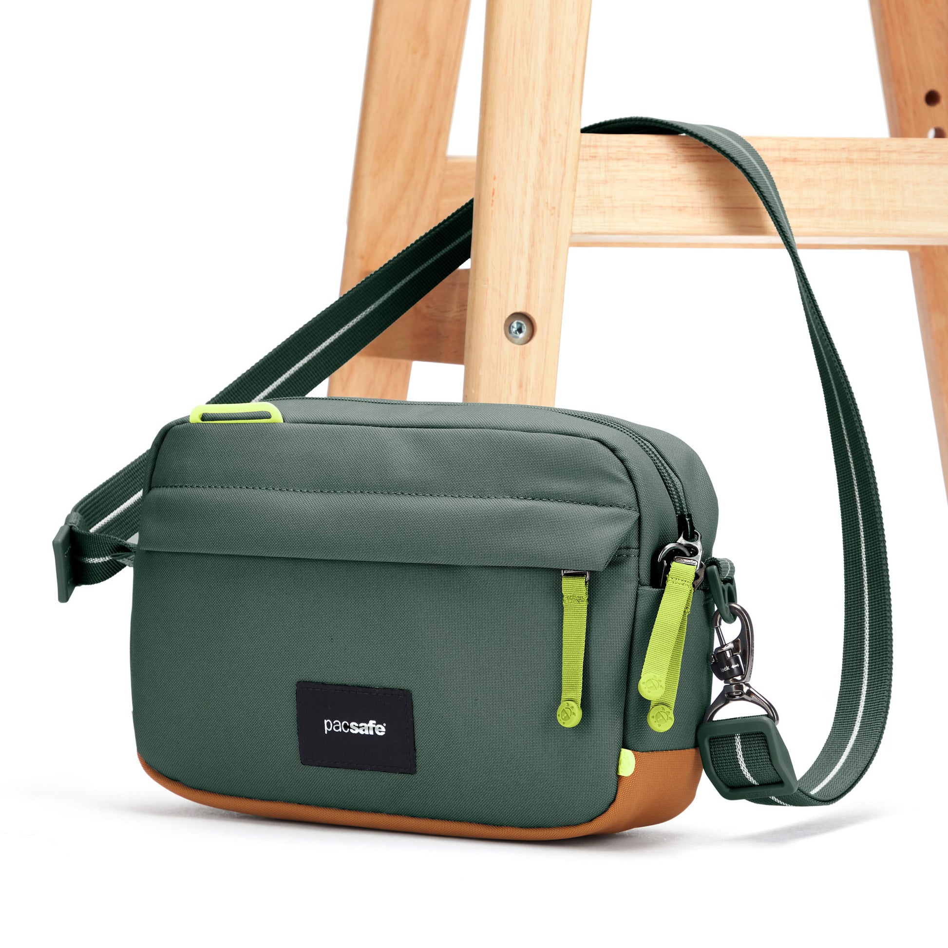 Pacsafe® GO Anti-Theft Crossbody Bag, spruce green, with crossbody strap affixed through wooden chair leg.