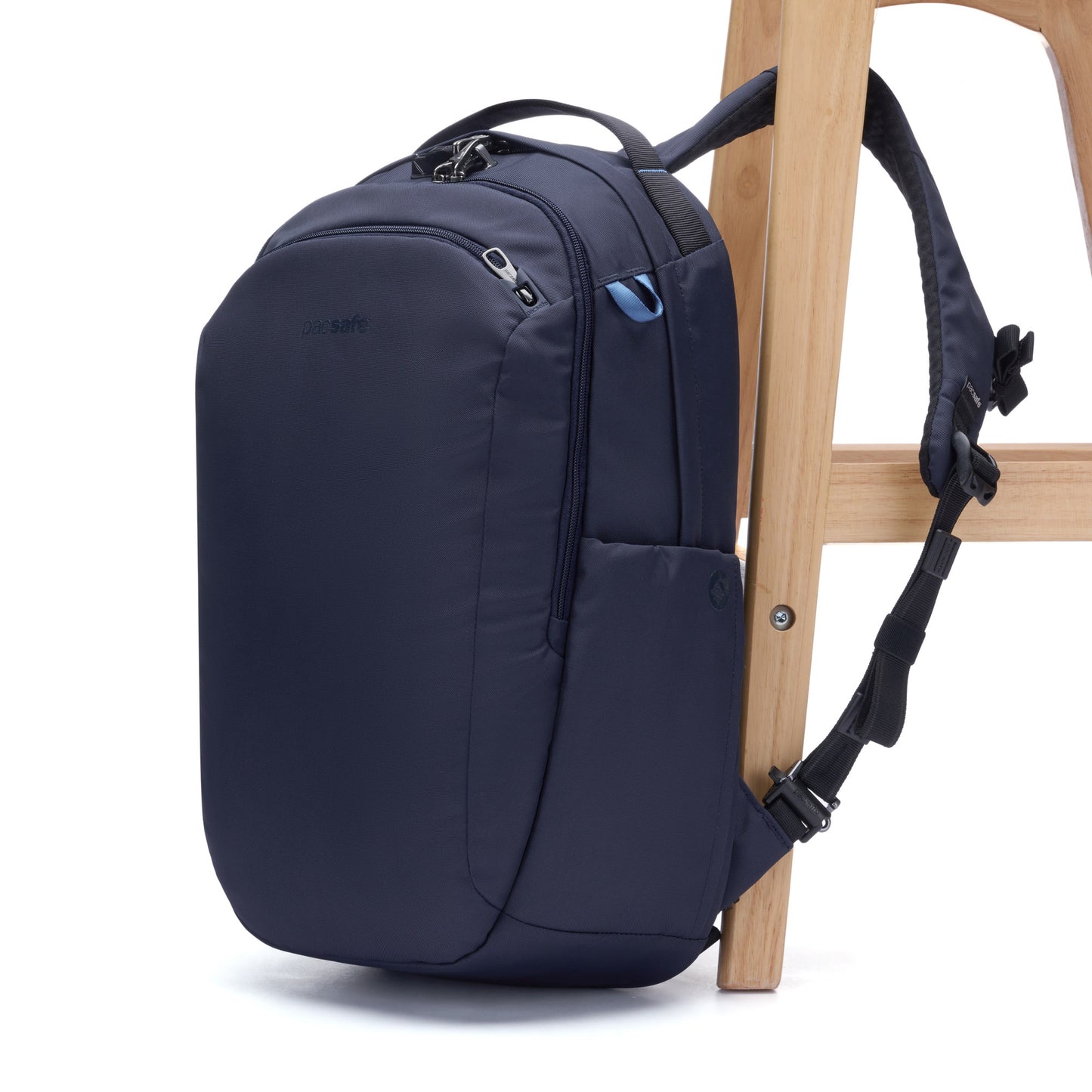 The Pacsafe V 26L Anti-theft Tour Backpack in ocean blue is secured to a wooden chair with its strap.