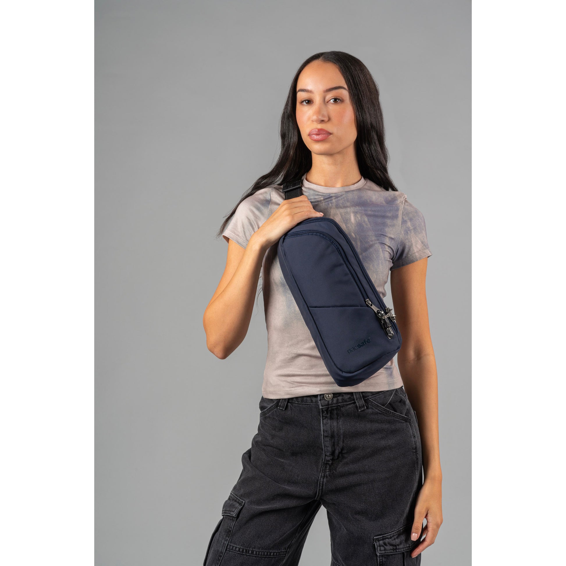 Woman wearing t-shirt and jeans with the ocean Pacsafe® V Anti-theft Action Sling Pack across her front.