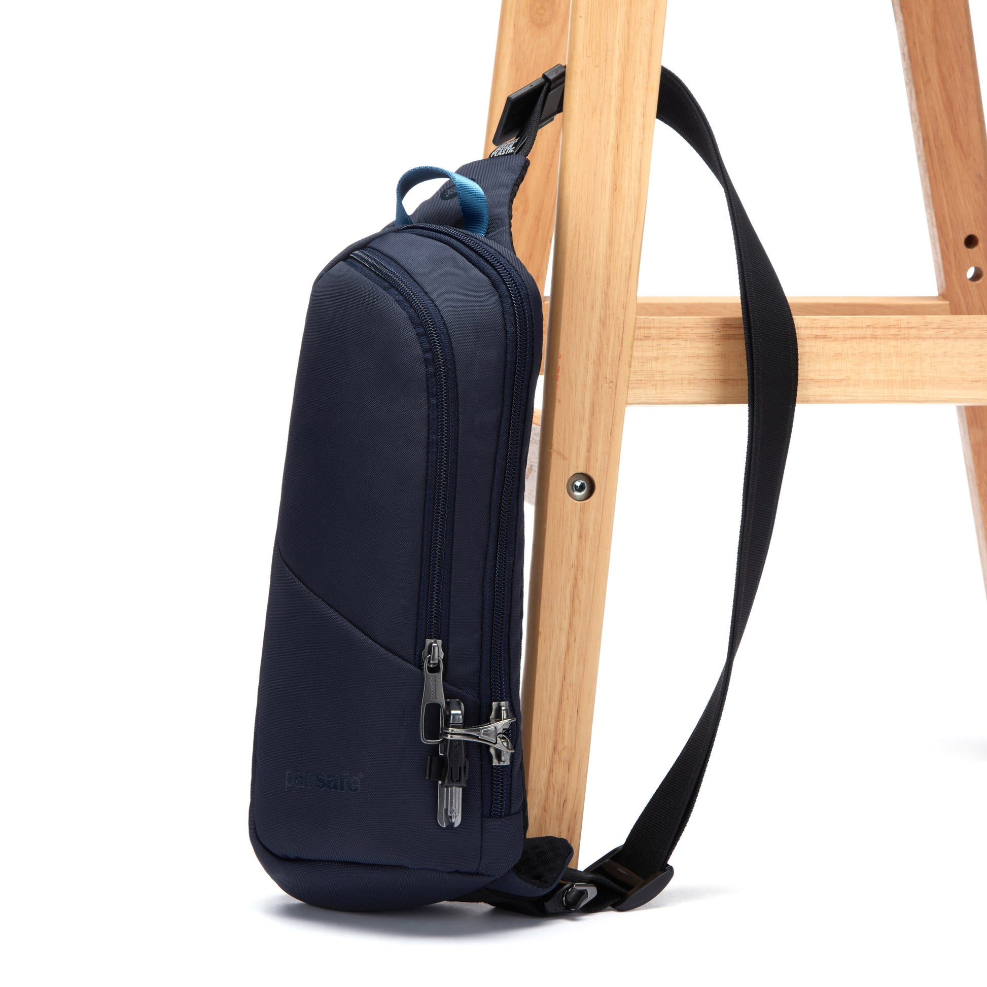 Pacsafe® V Anti-theft Action Sling Pack in ocean, secured to wooden leg of stool.