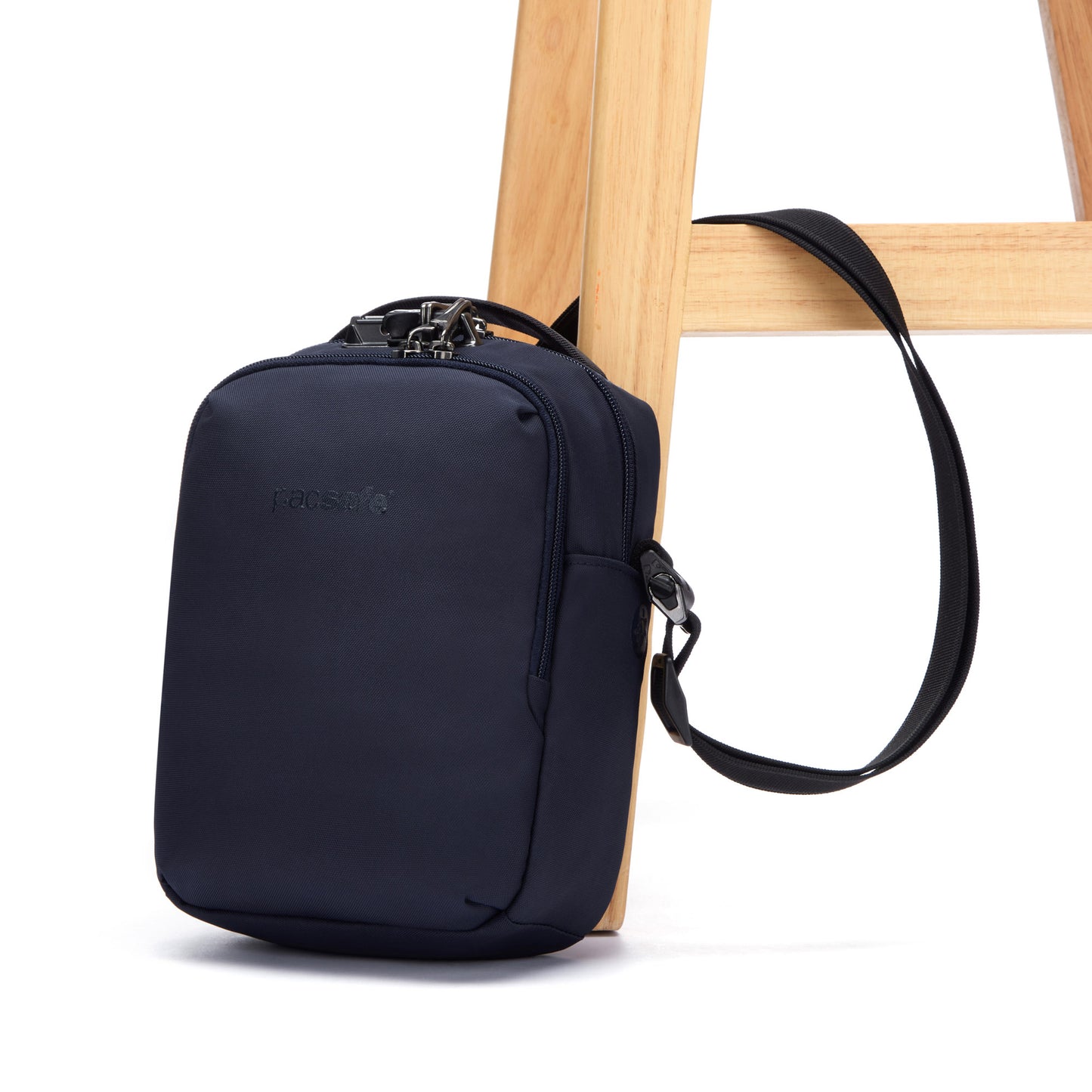 Pacsafe® V Anti-theft Companion Crossbody bag in recycled polyester hangs on a wooden chair leg.