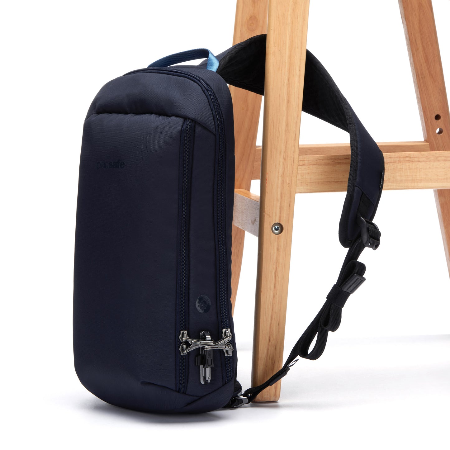 A Pacsafe® V Tech Anti-theft Sling Pack rests against a wooden ladder on a white backdrop.