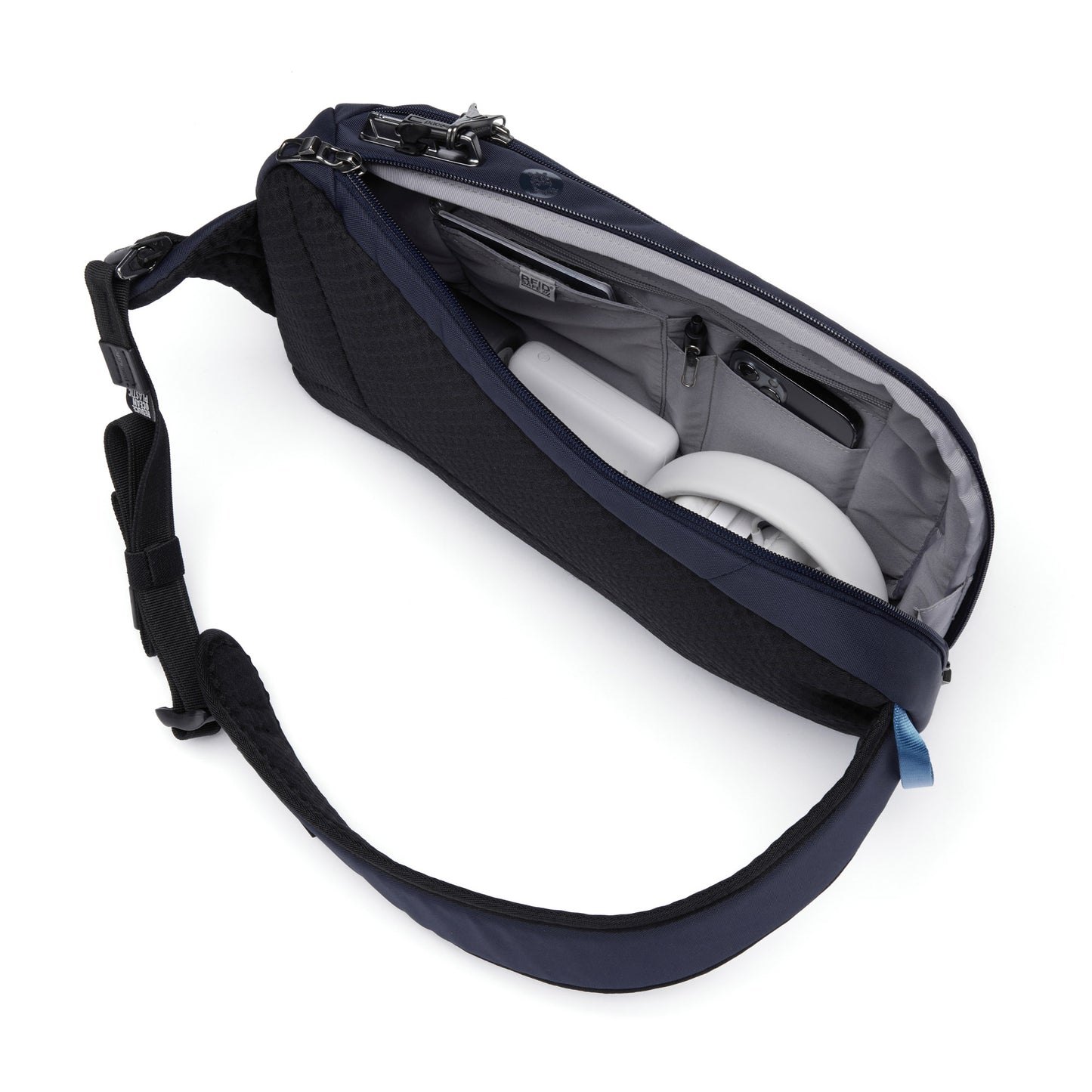Pacsafe® V Tech Anti-theft Sling Pack with open zipper, showcasing a passport, phone, headphones and charger inside.