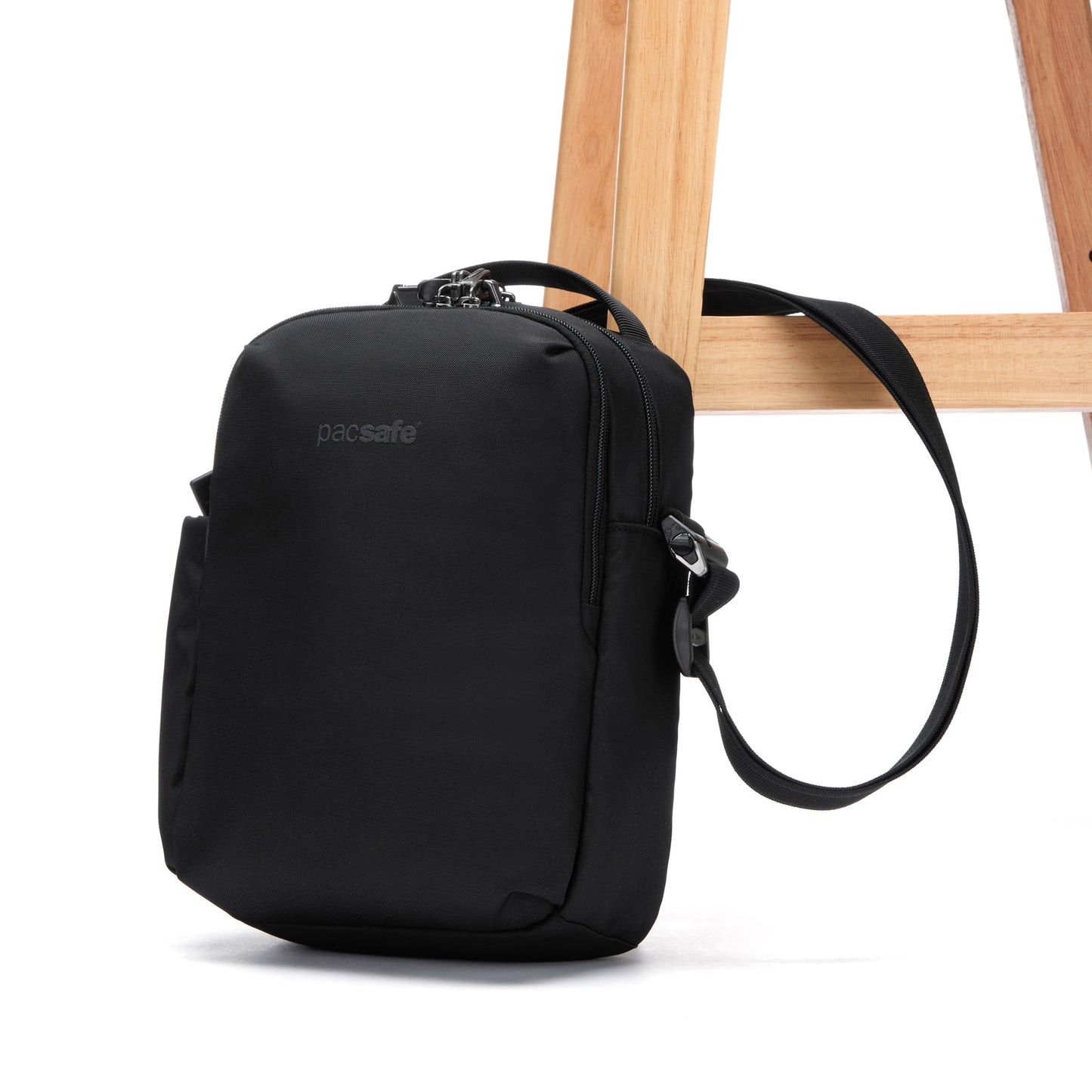 The Pacsafe® V Anti-theft Tour Crossbody from Pacsafe attached to a wooden chair leg.