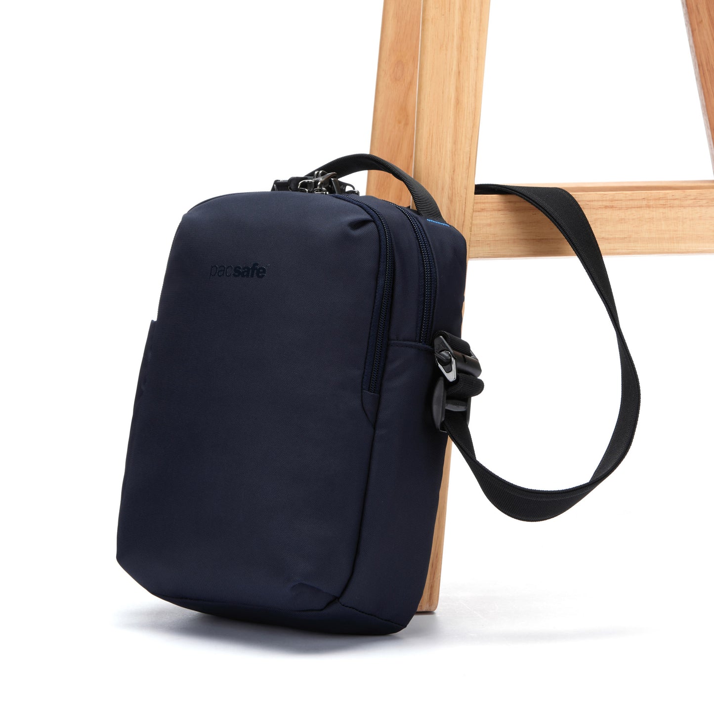 A Pacsafe® V Anti-theft Tour Crossbody in ocean blue, with lockable compartments, attached to a chair leg.