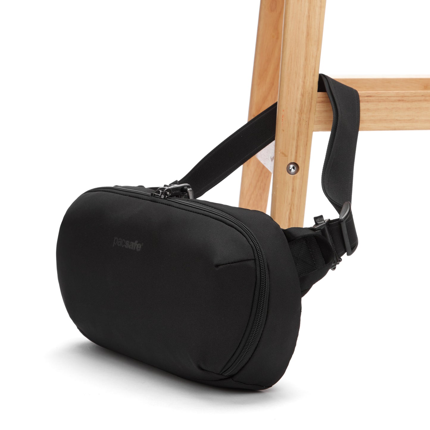 The Pacsafe® V Anti-theft Urban Sling, a black bag, hangs on a wooden chair.