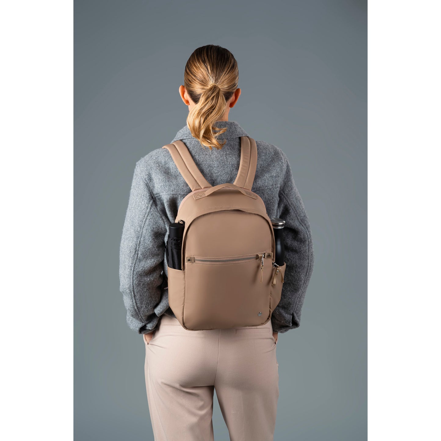 Back view of a woman wearing a grey jacket and the taupe Pacsafe W Backpack
