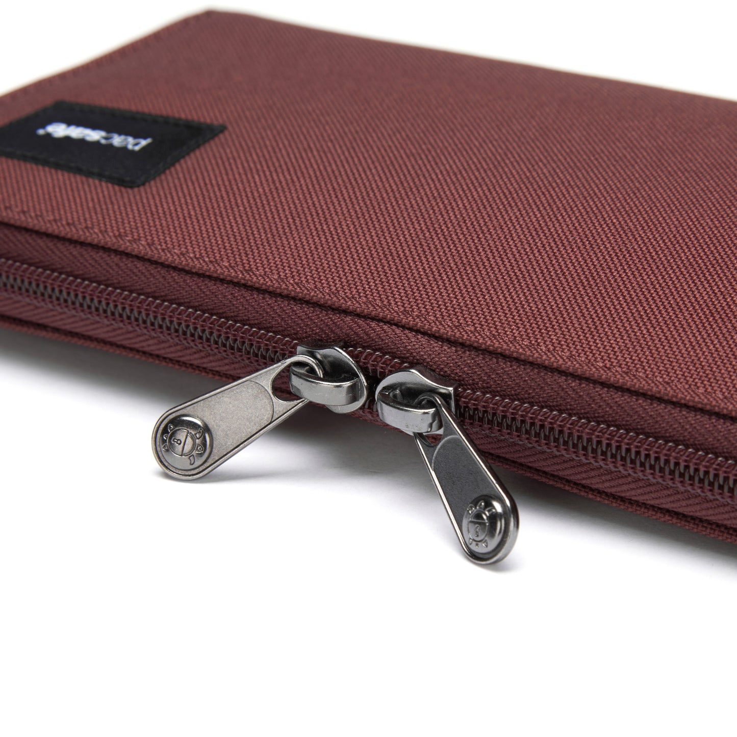 Close-up of a garnet red Pacsafe® wallet made from recycled polyester with dual zippers and a black logo patch.