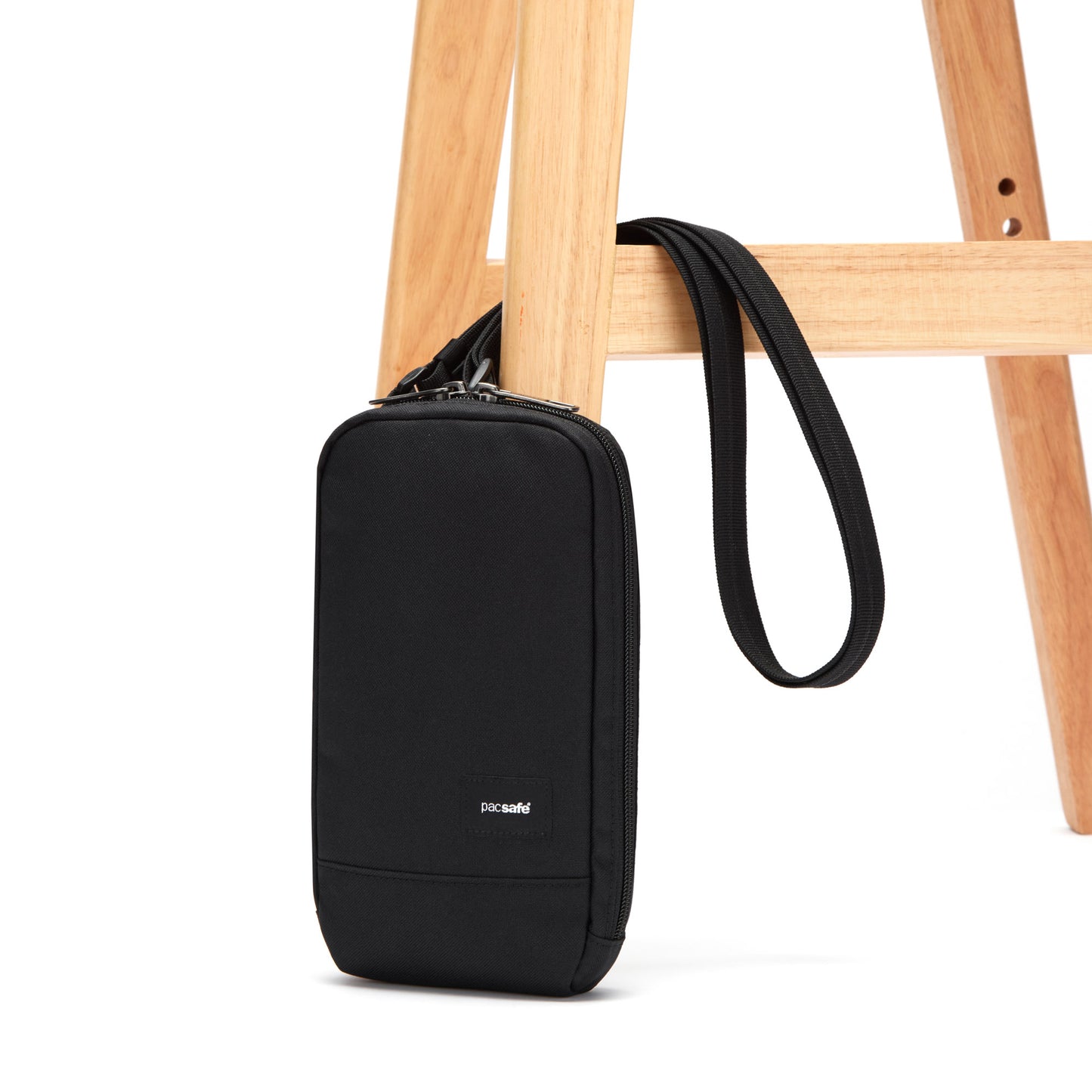 Pacsafe® RFIDsafe™ crossbody bag made with recycled polyester, hanging from a wooden chair.