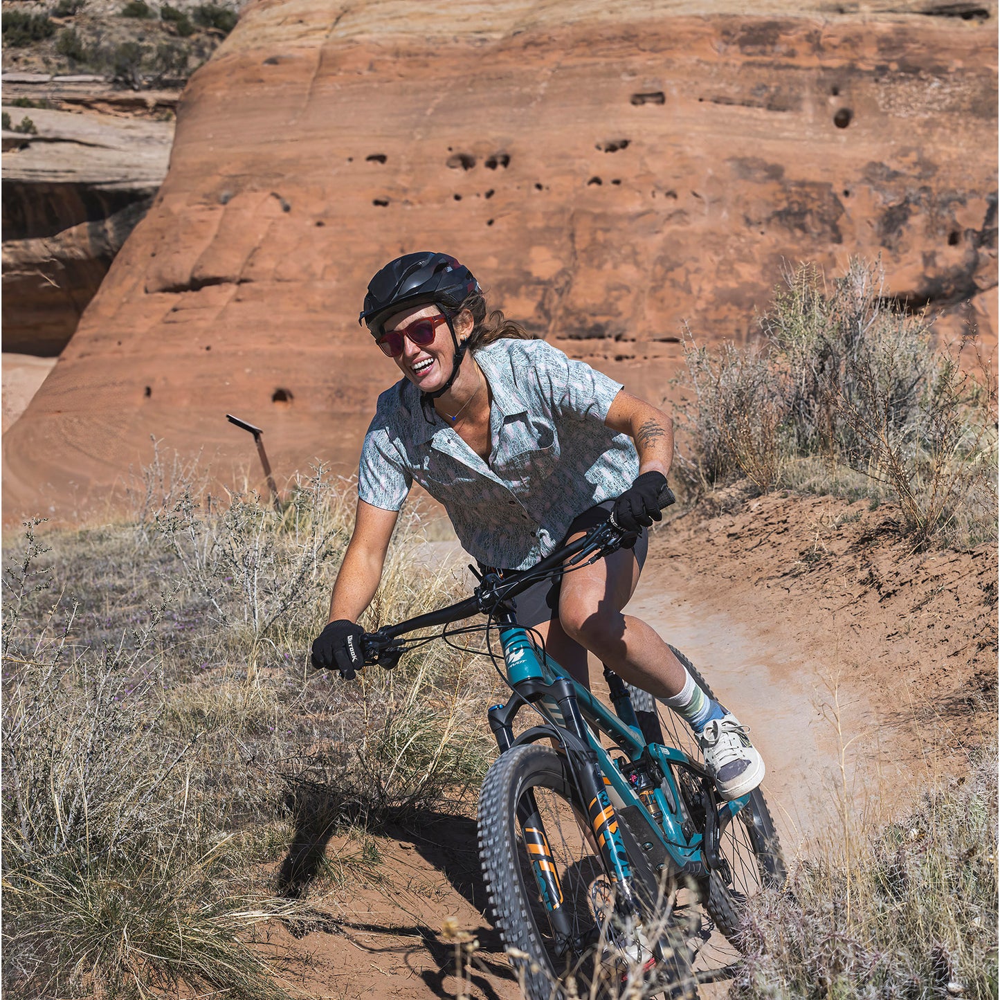 Lifestyle image of woman riding a bike in the desert wearing the Royal Robbins Camino short sleeve shirt.