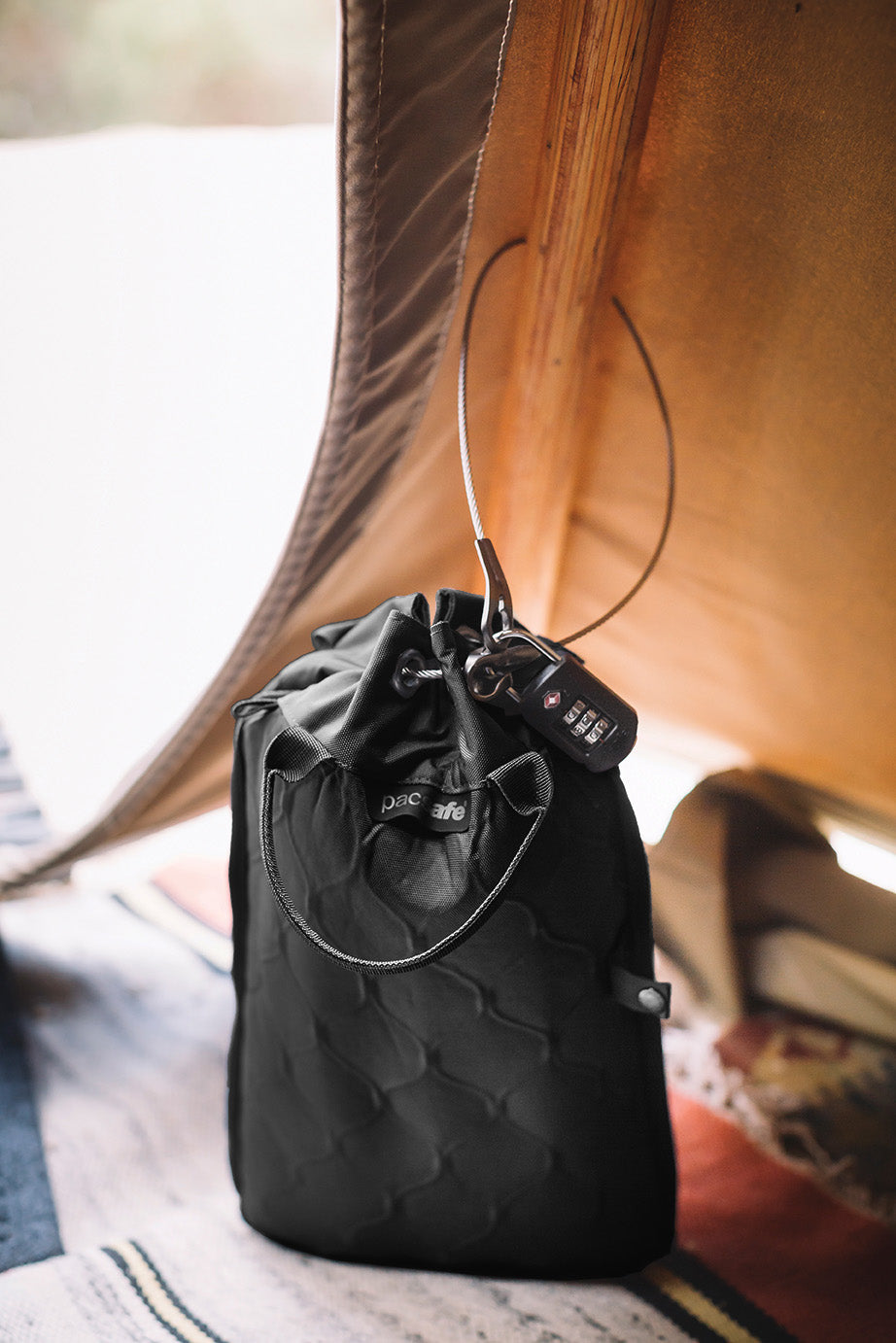 Pacsafe® Travelsafe® 3L GII Anti-Theft Portable Safe, recycled black quilt with drawstring, on blanket by a tent.