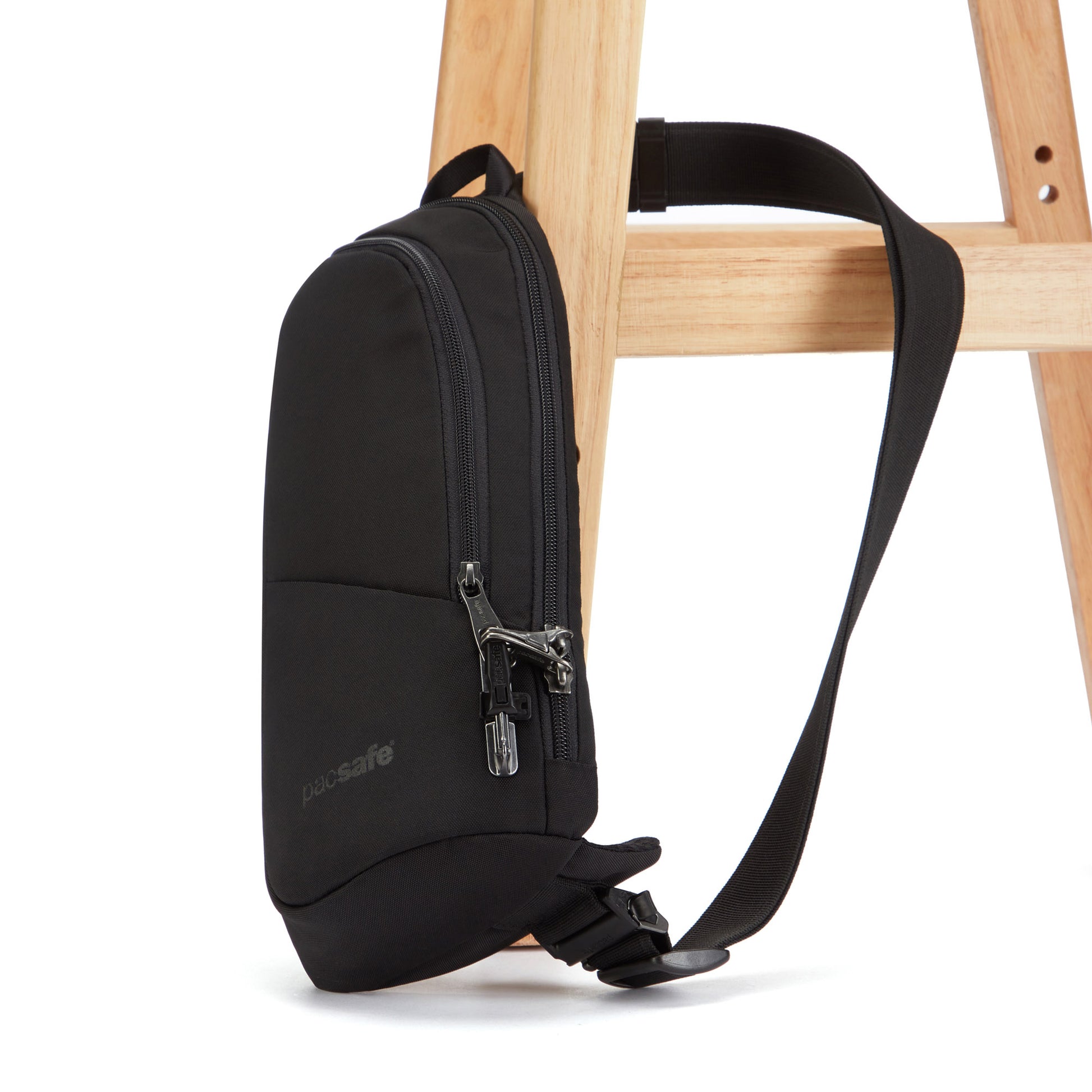 Pacsafe® V Anti-theft Action Sling Pack in recycled polyester with zipper, hanging on a wooden chair.