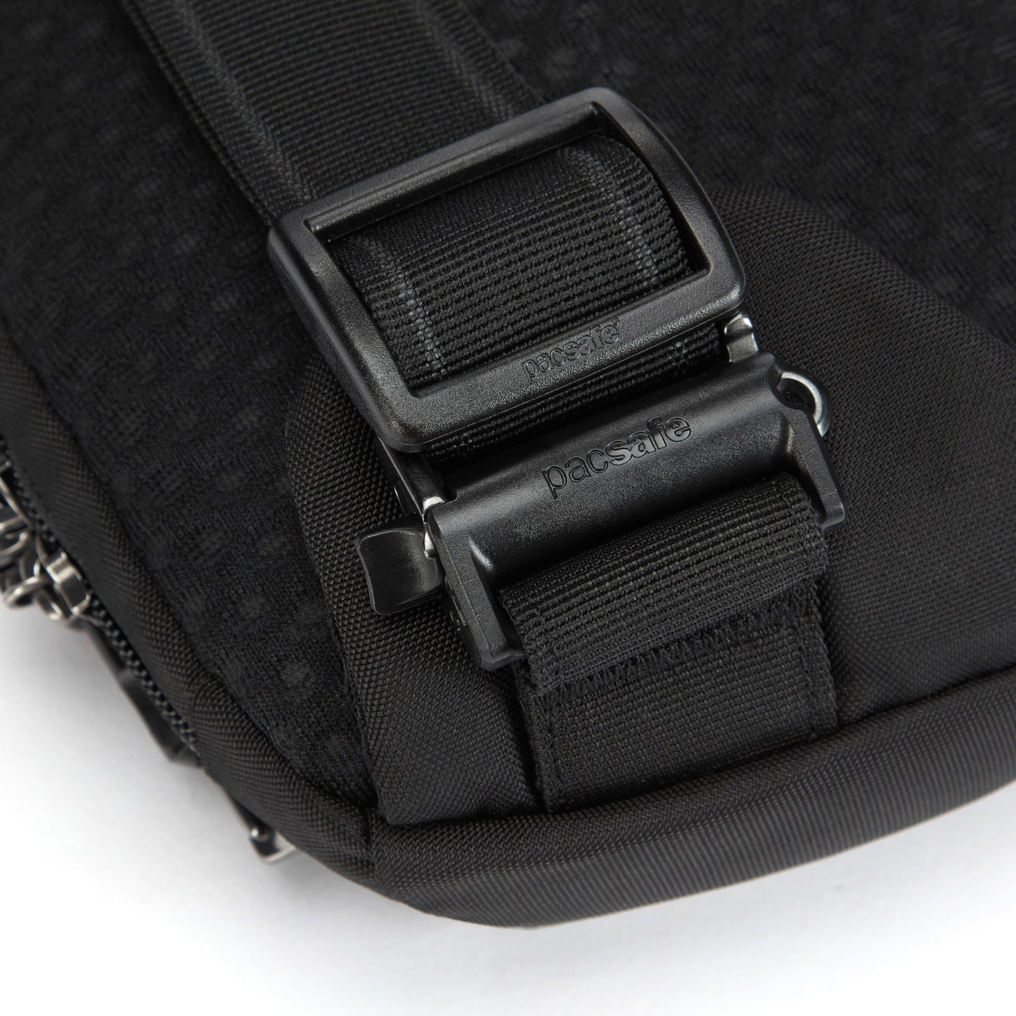 Close-up of Pacsafe® V Sling Pack with black strap, plastic buckle, and metal clip on textured fabric.