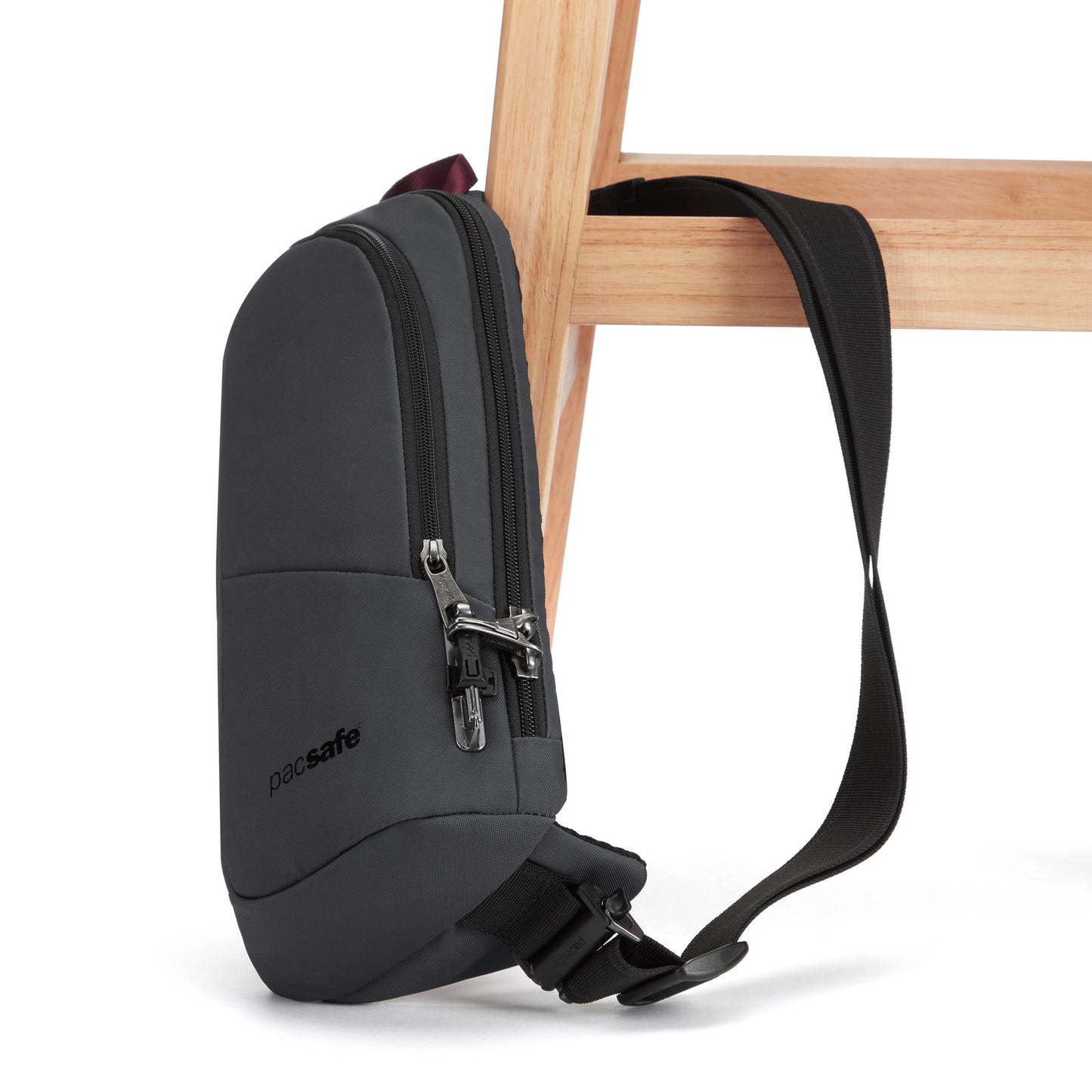 The Pacsafe® V Anti-theft Action Sling Pack in slate, made of recycled polyester, hangs from a wooden chair.